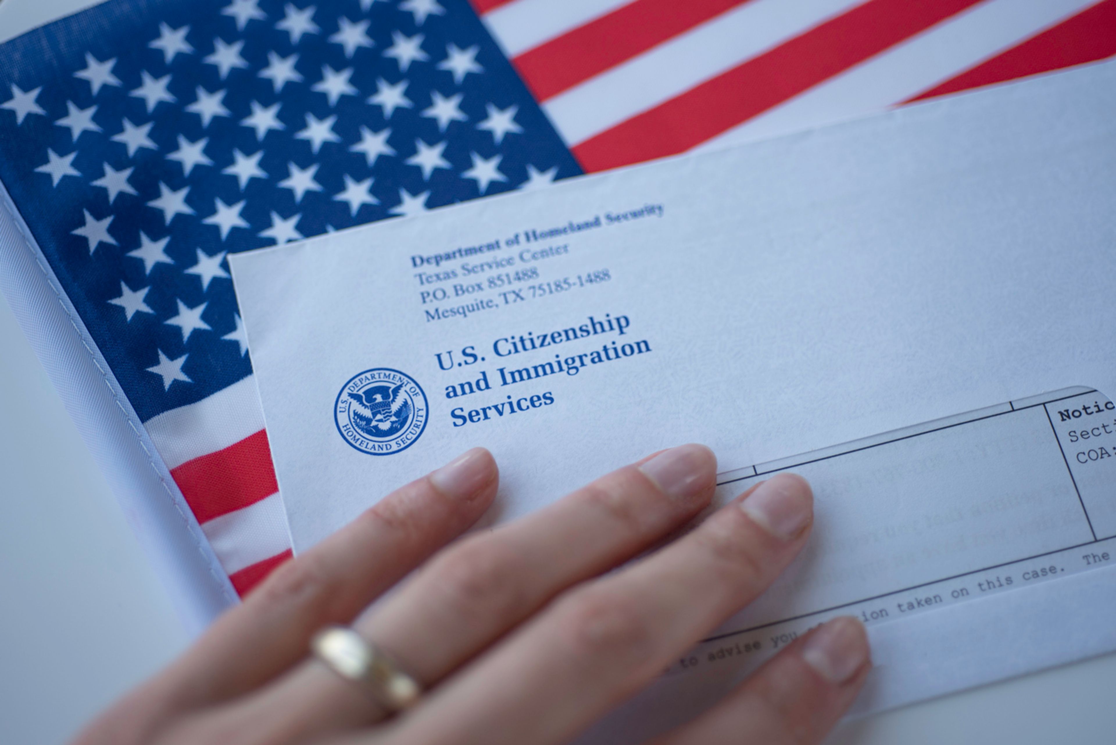 A white hand rests on top of an envelope from USCIS.