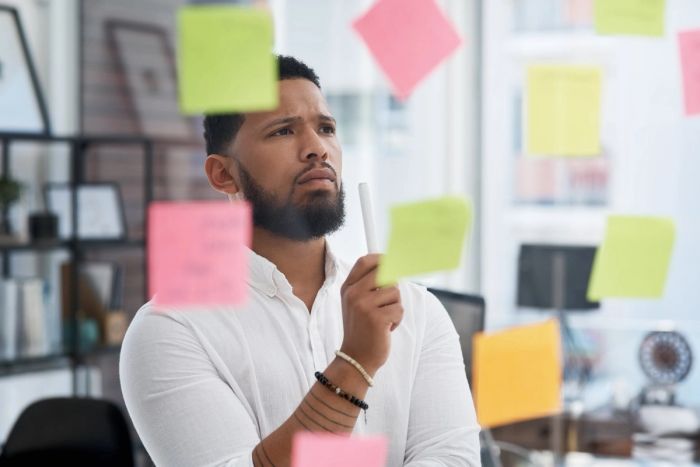 A businessman looks at sticky notes on a glass wall as he tries to decide between multiple options.