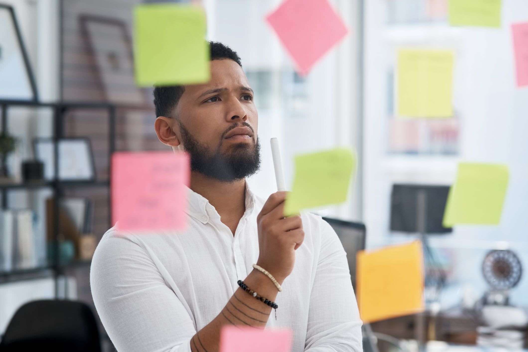 A businessman looks at sticky notes on a glass wall as he tries to decide between multiple options.
