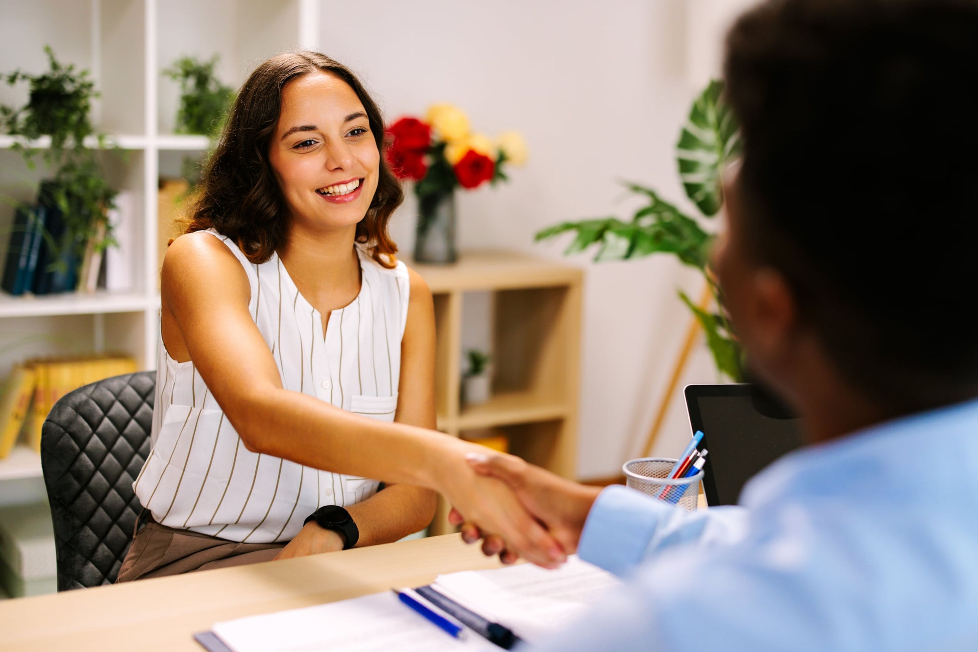 A young woman sits in front of a desk and shakes hands with an immigration officer during an F-1 student visa interview.