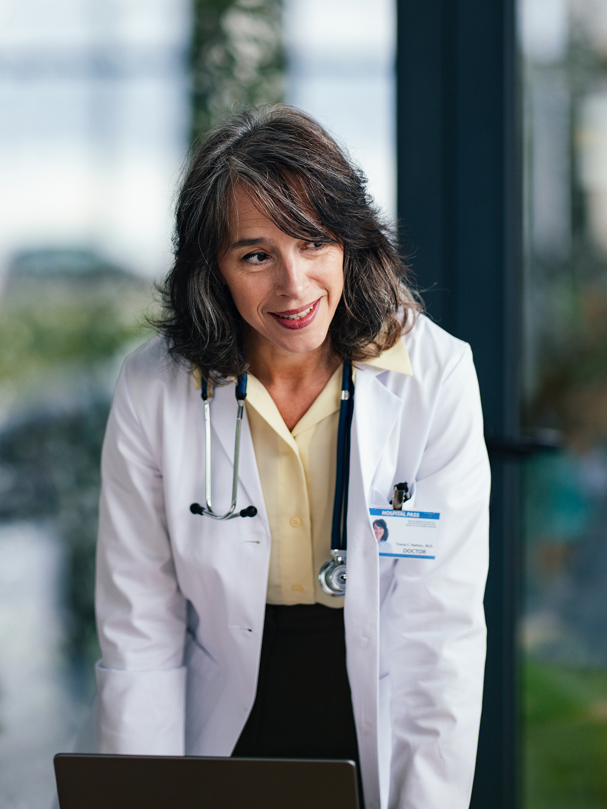 A physician in a lab coat smiling while working at a laptop