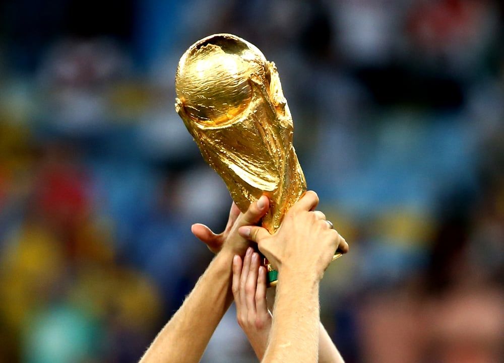 Close-up of World Cup being held up by several people's hands.