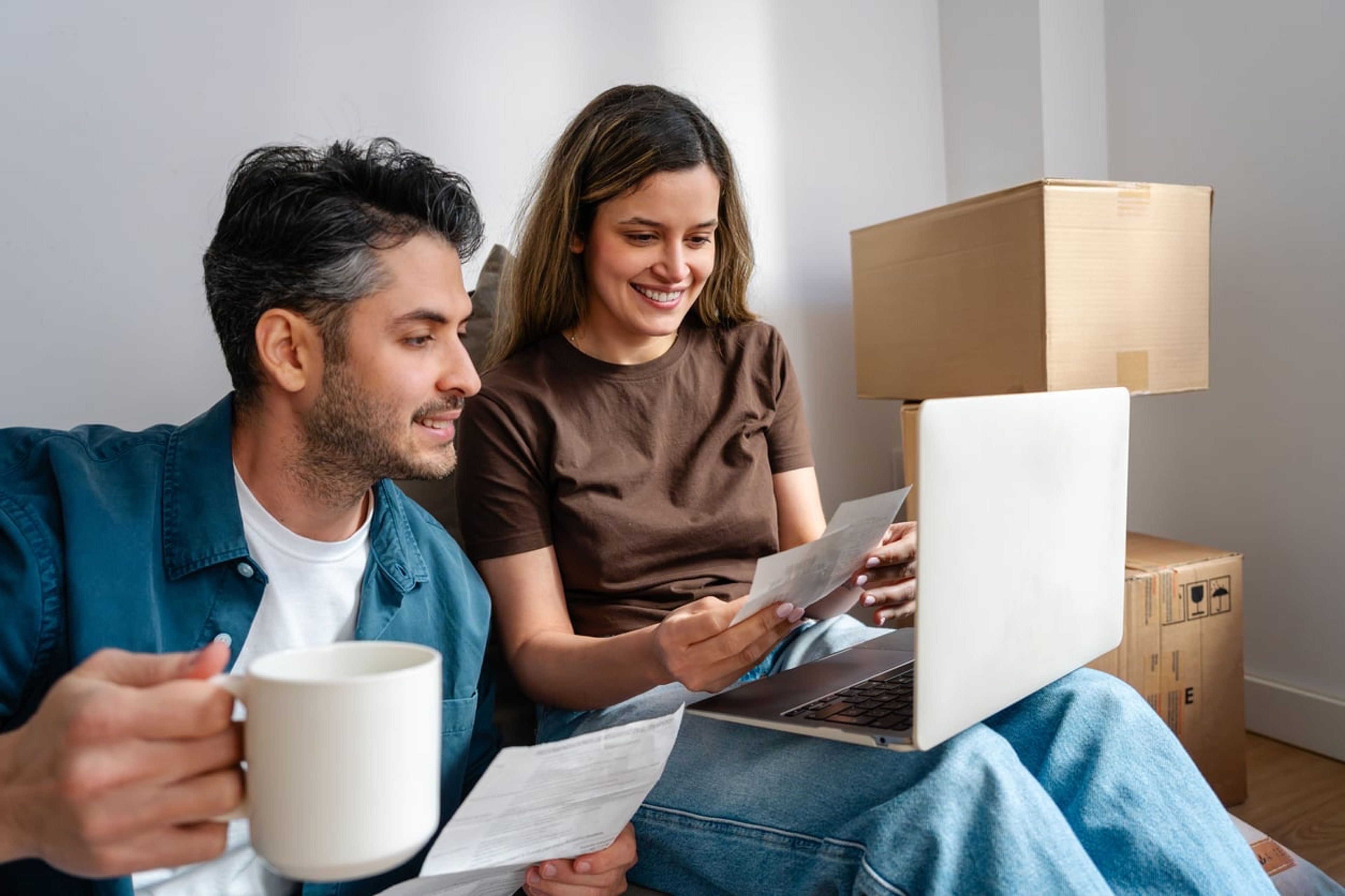 A young couple sitting next to boxes is looking at Form AR-11 to change their address with USCIS.