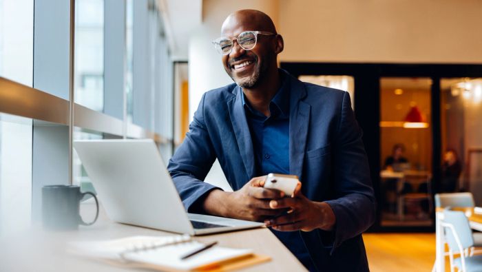 Businessman in office smiling while looking up from his laptop.