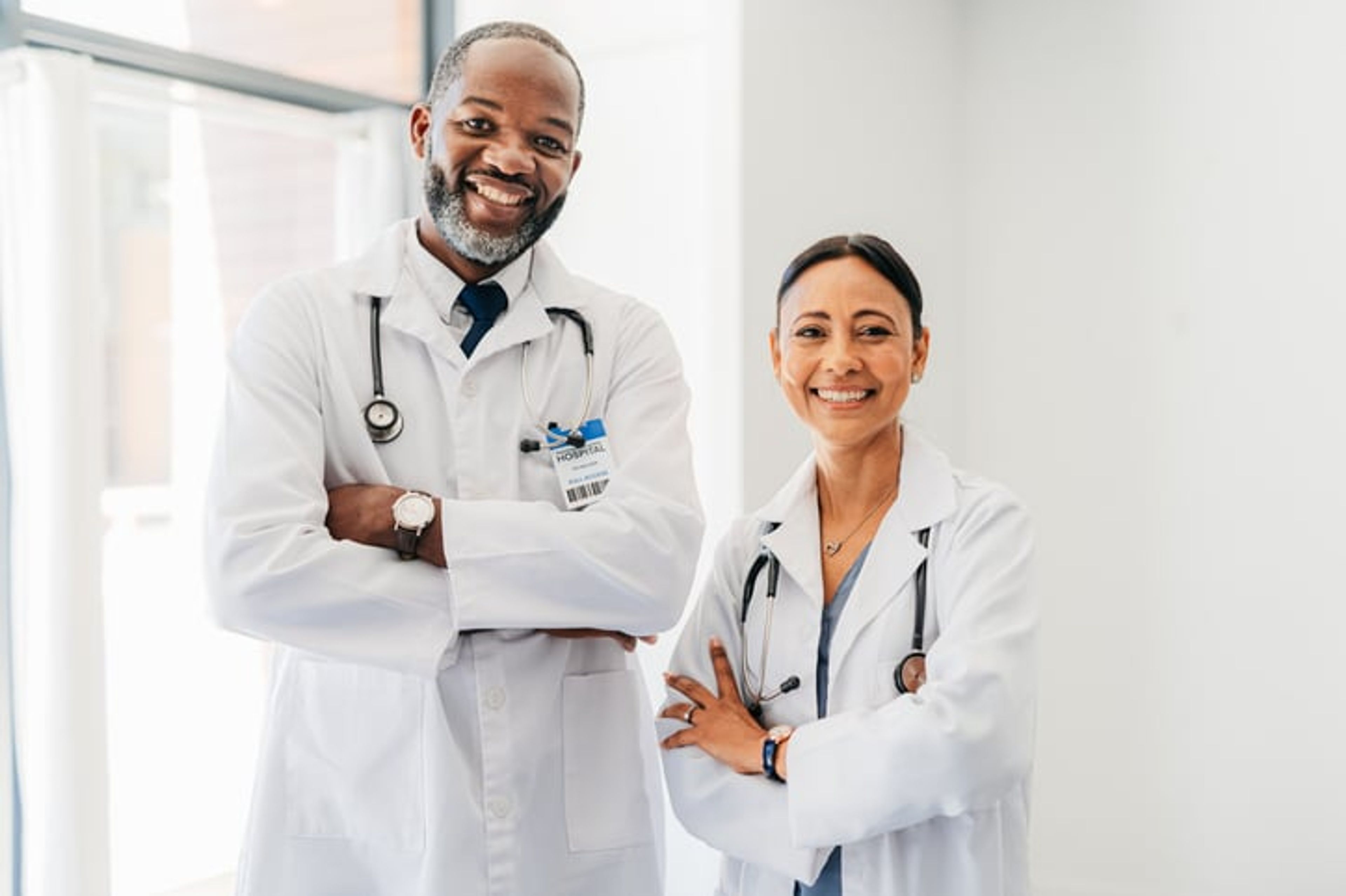 Two doctors stand side by side smiling.