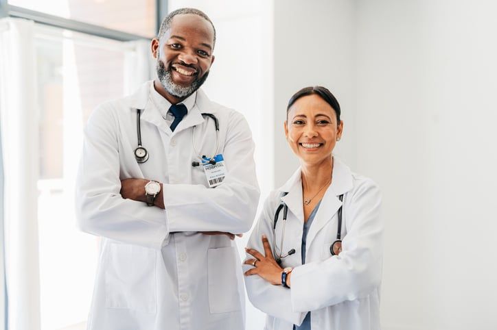 Two doctors stand side by side smiling.