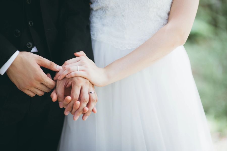 Close-up of a bride and groom holding hands, both wearing wedding bands.