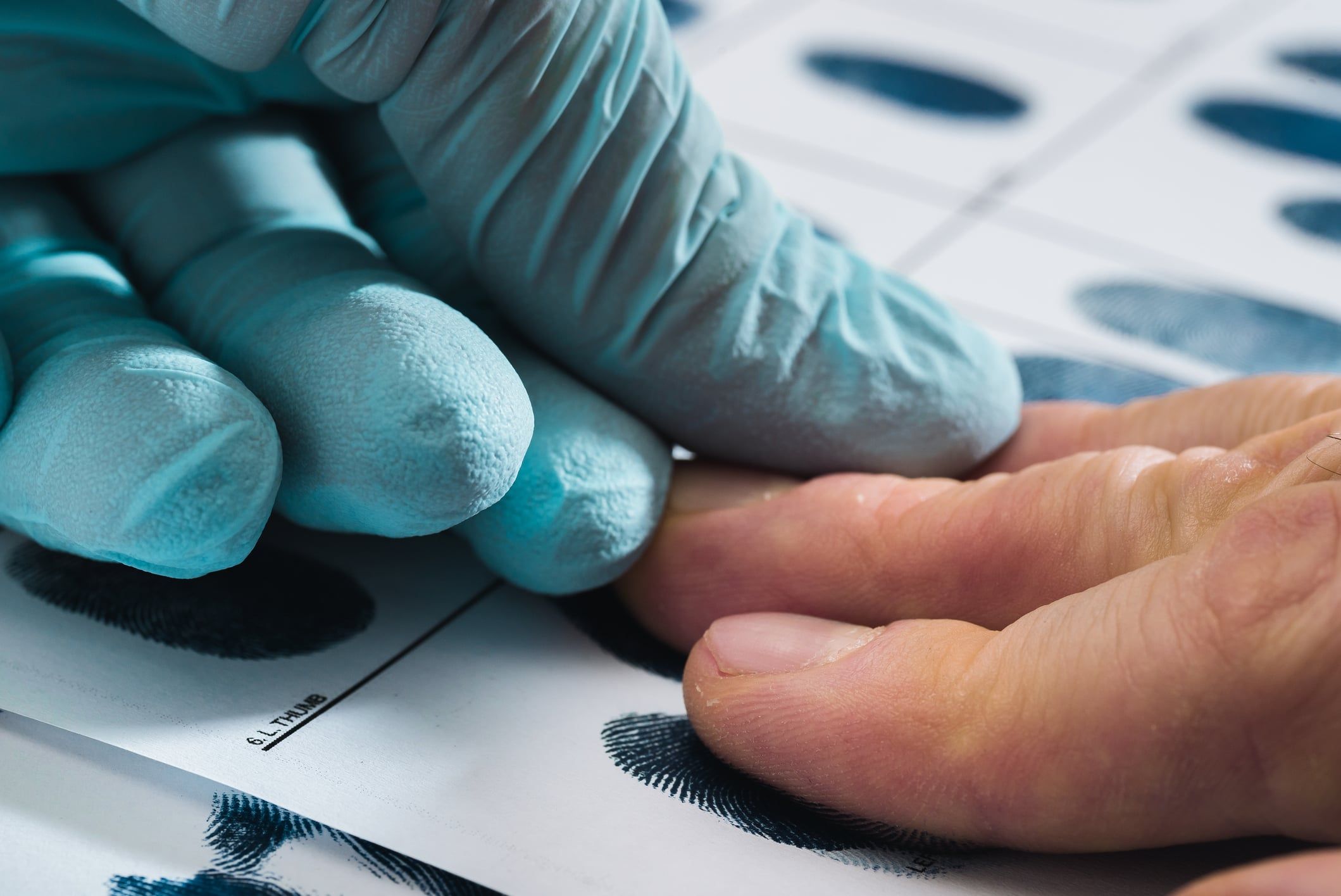 A gloved hand taking fingerprints of another hand during a USCIS biometrics appointment.