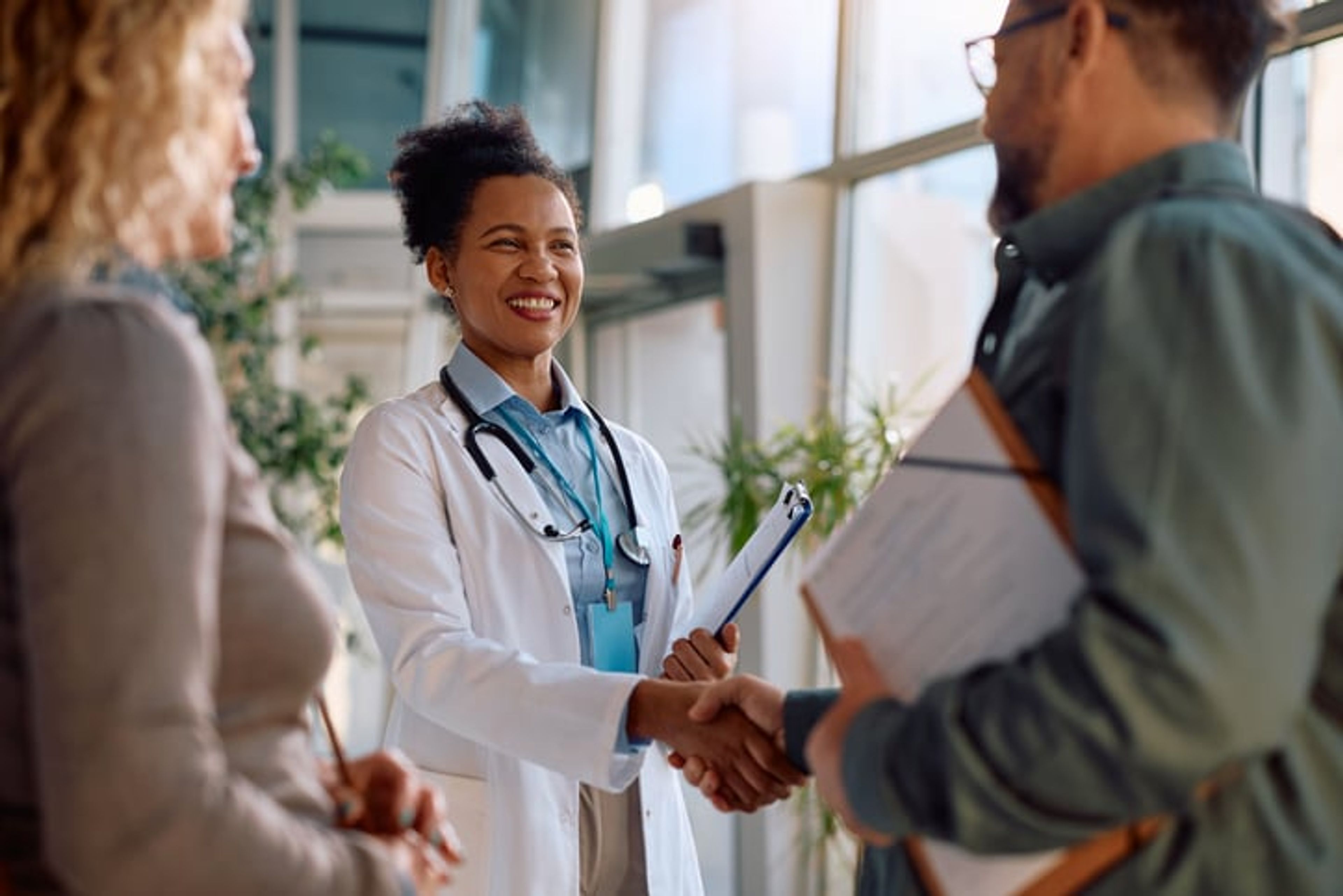 A smiling medical doctor shakes hands with someone at a clinic.