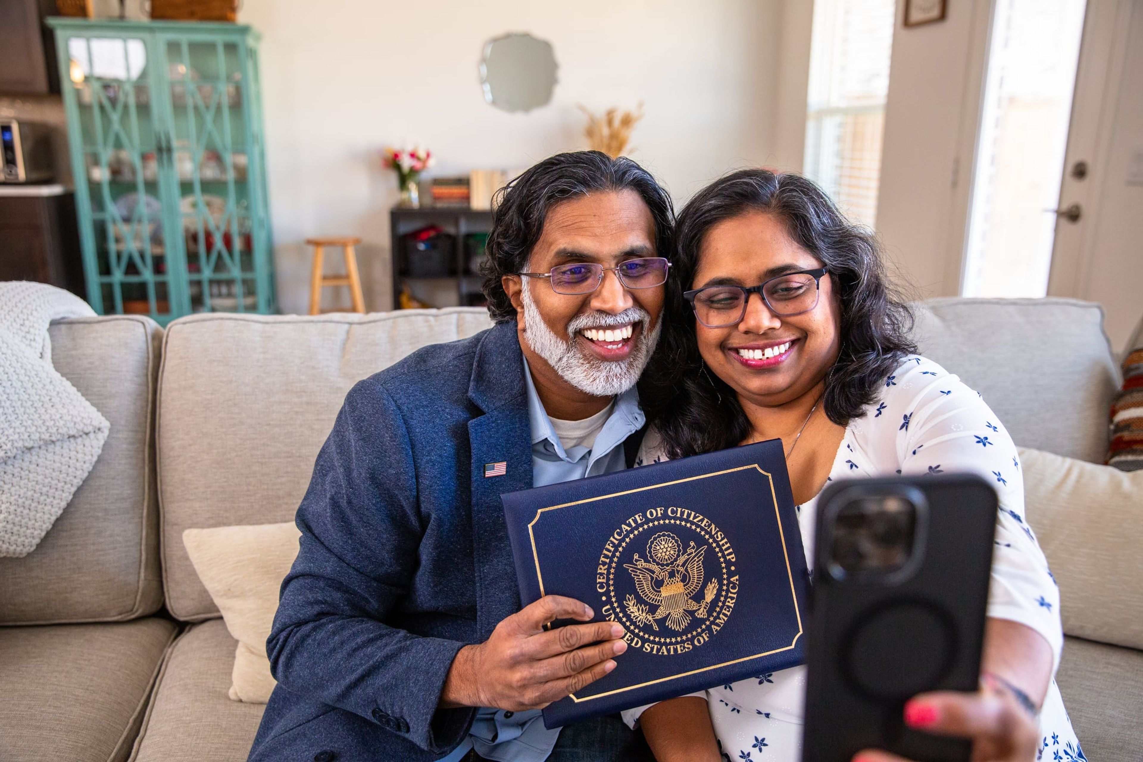 A proud immigrant couple holds up their Certifiicate of Citizenship on a video call with family.