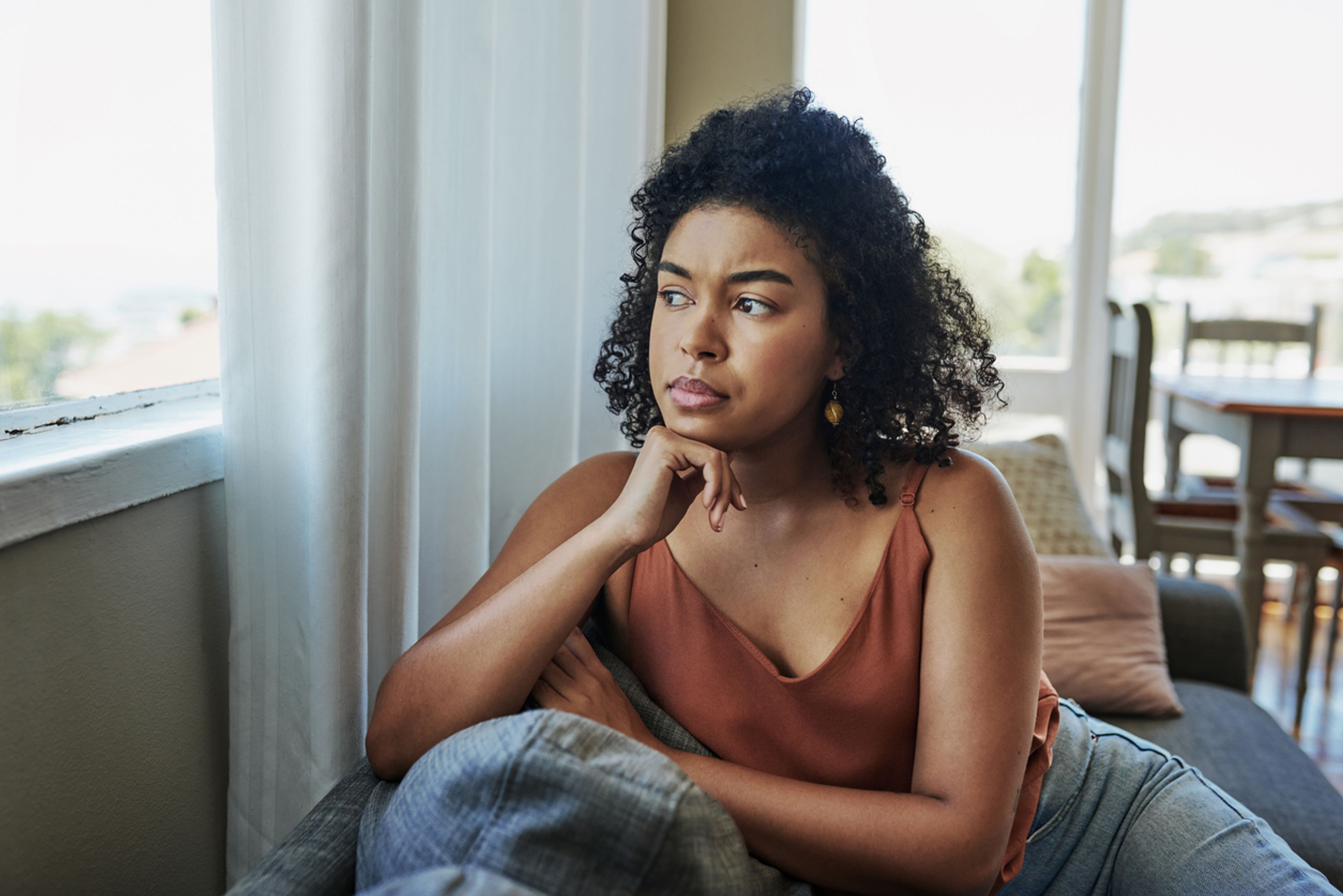 Young woman looking pensively out a window at home.