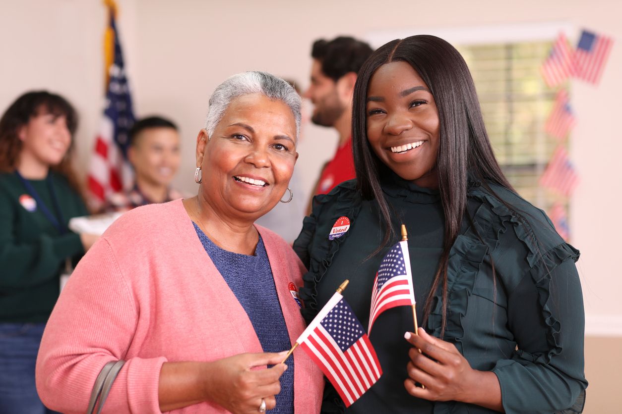 Two women holding flags and wearing an "I voted" sticker
