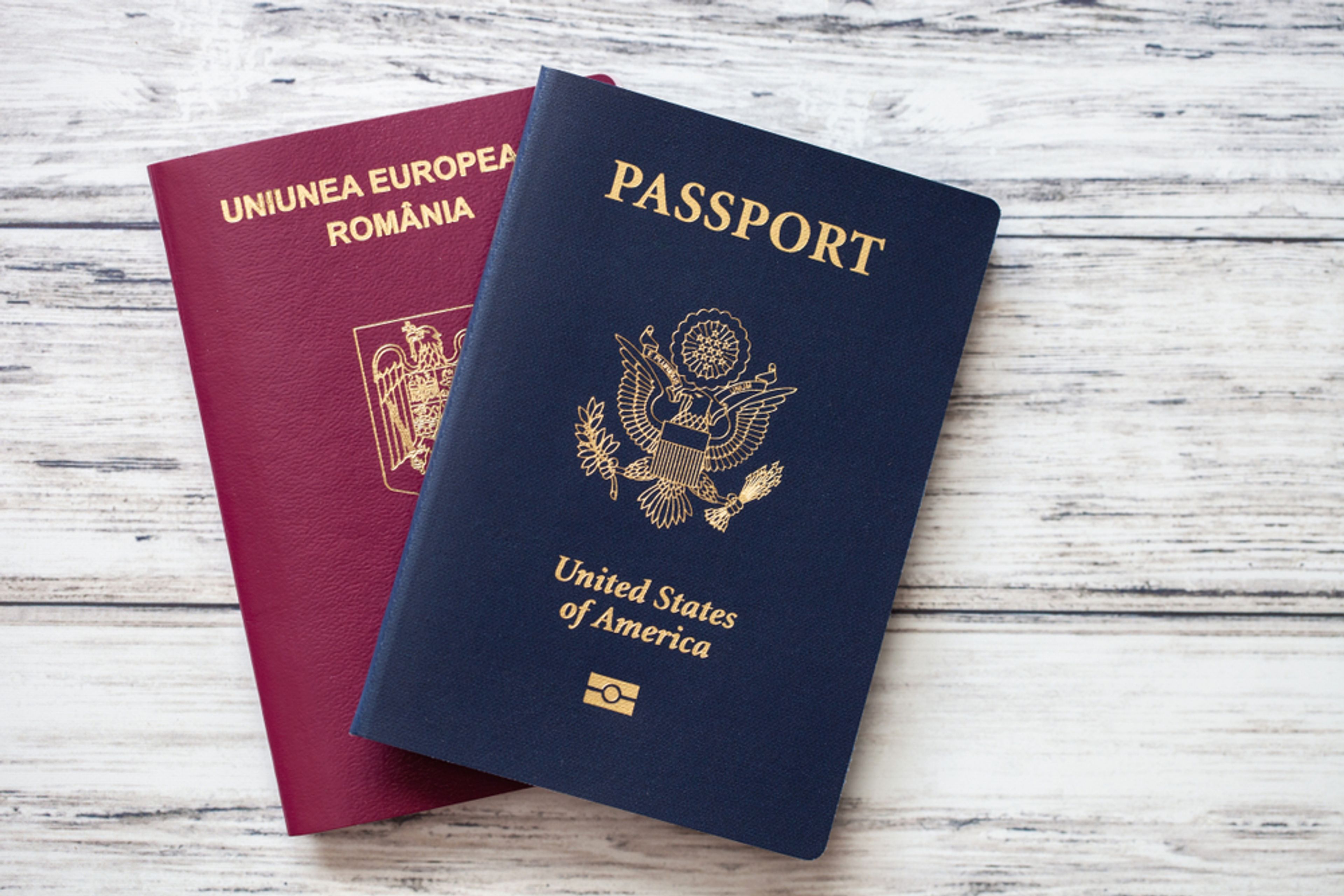 Two passports, one for the U.S. and one for Romania, laying on a white tabletop.