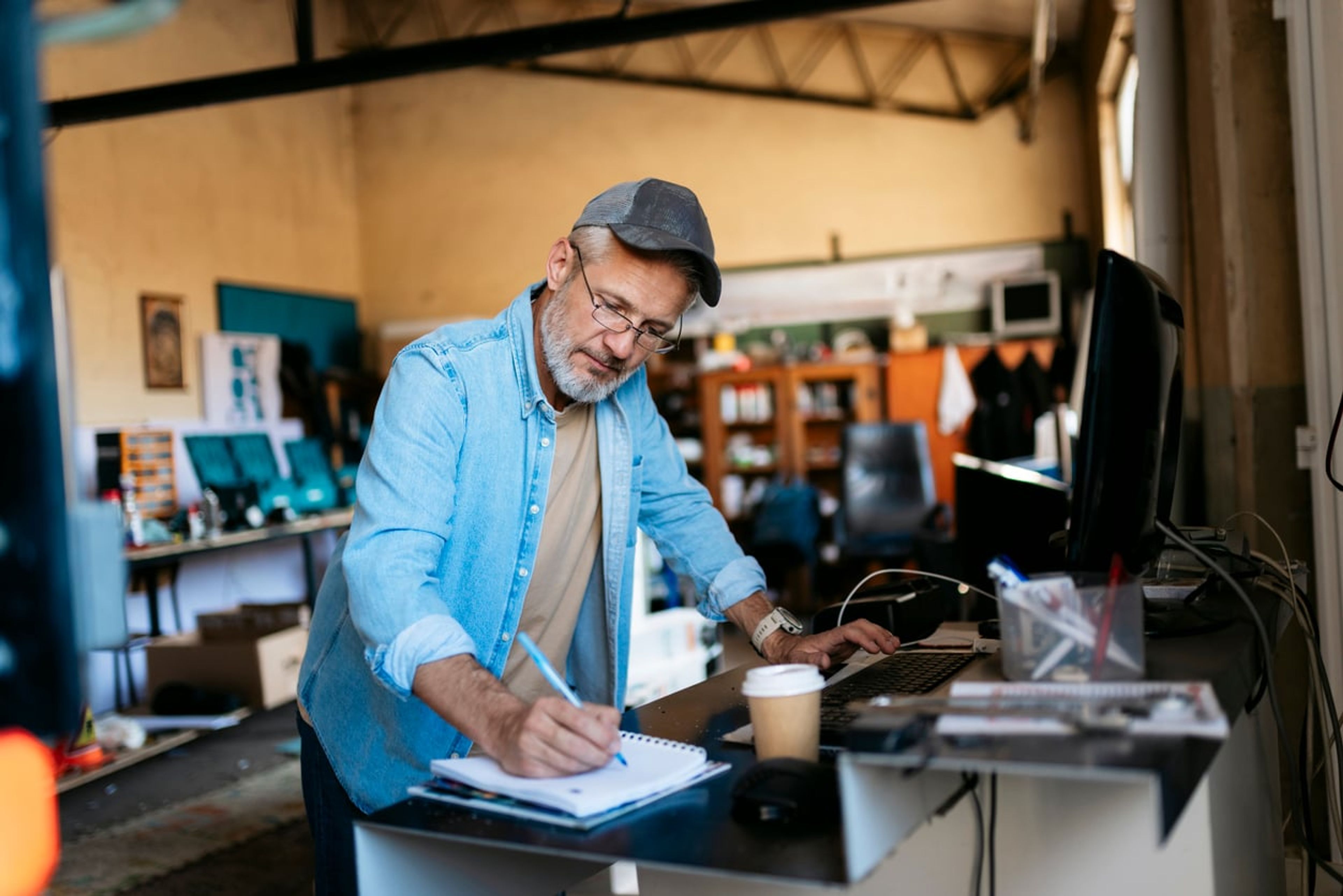 Small business owner working at the front desk of his workshop and taking notes in a notepad.