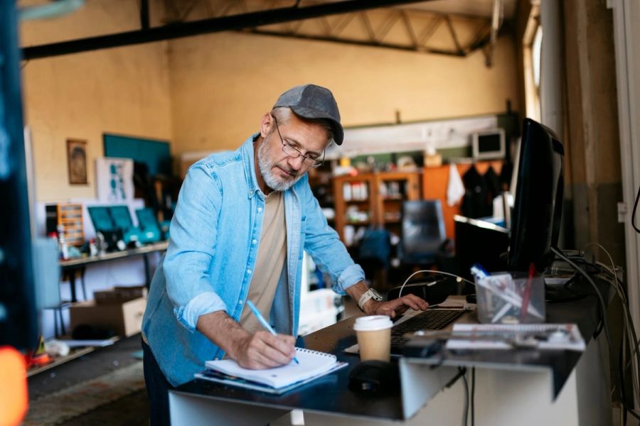 Small business owner working at the front desk of his workshop and taking notes in a notepad.