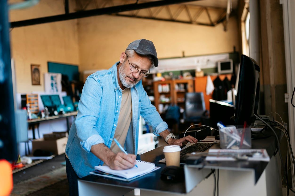 Small business owner working at the front desk of his workshop and taking notes in a notepad.