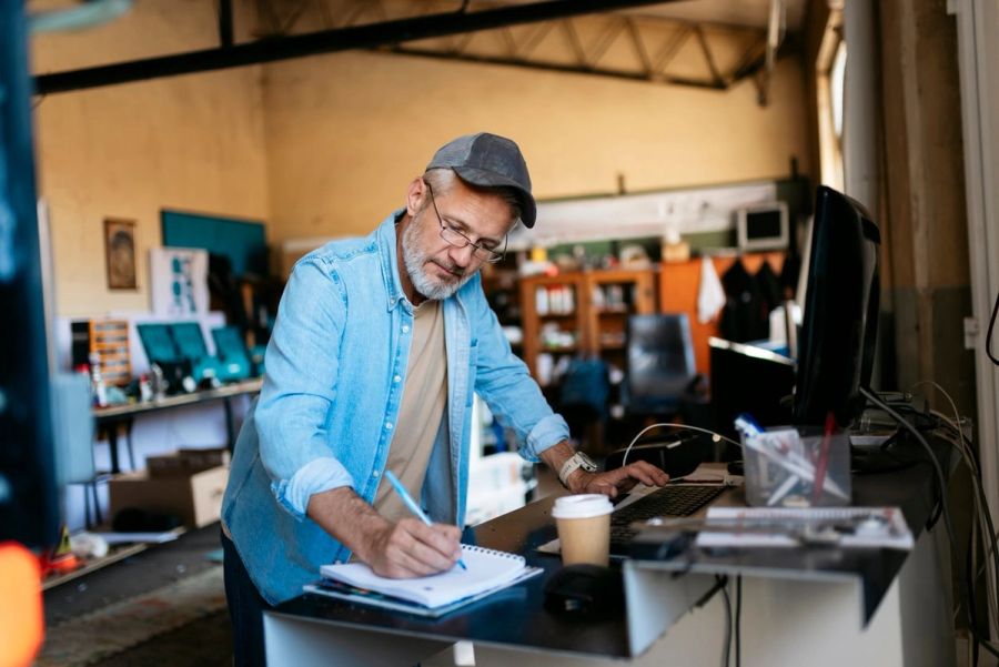 Small business owner working at the front desk of his workshop and taking notes in a notepad.