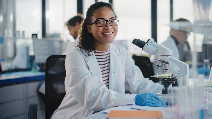 A medical exchange visitor sits in front of a microscope smiling.