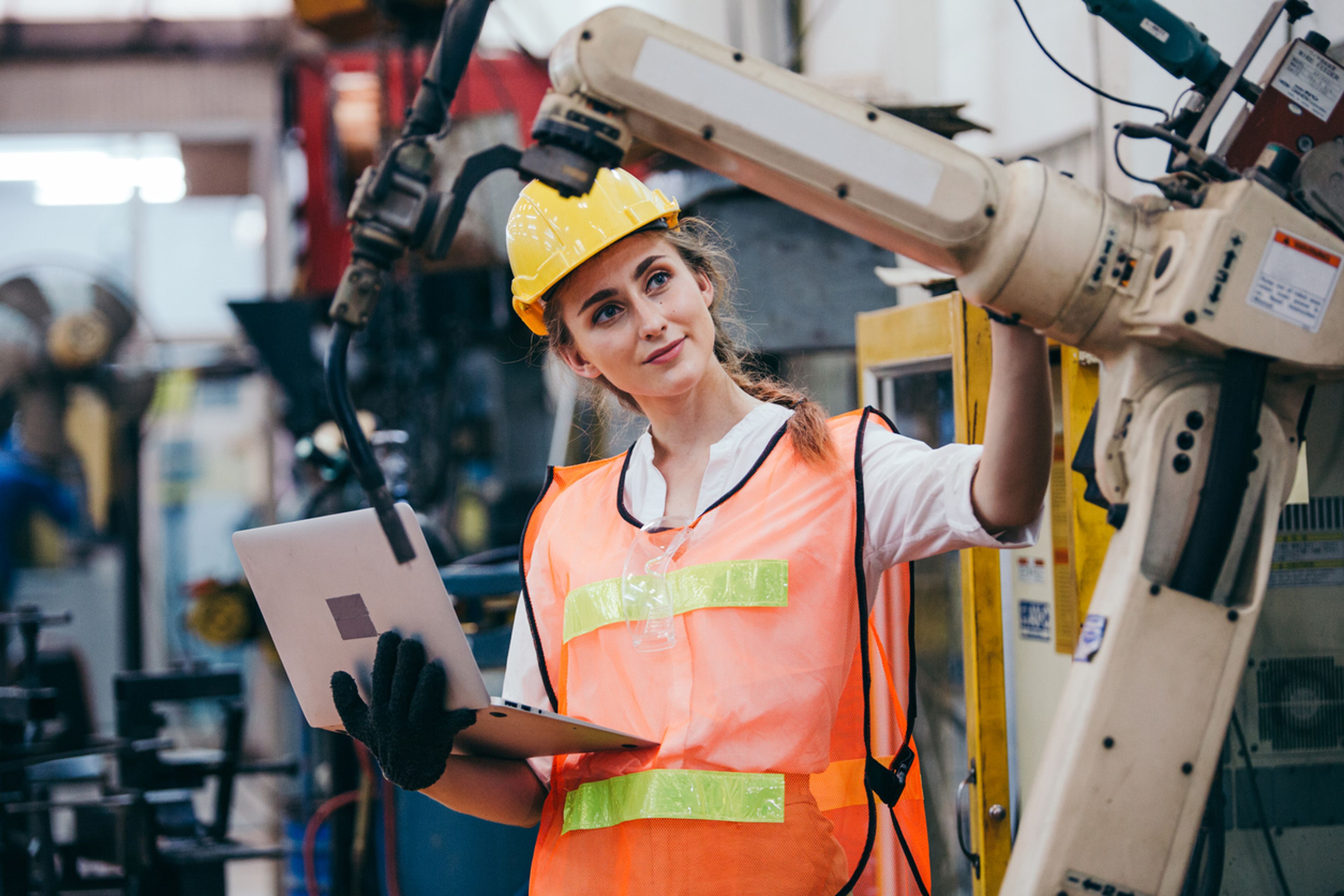 Industrial engineer using laptop checking on robotic arm machine.