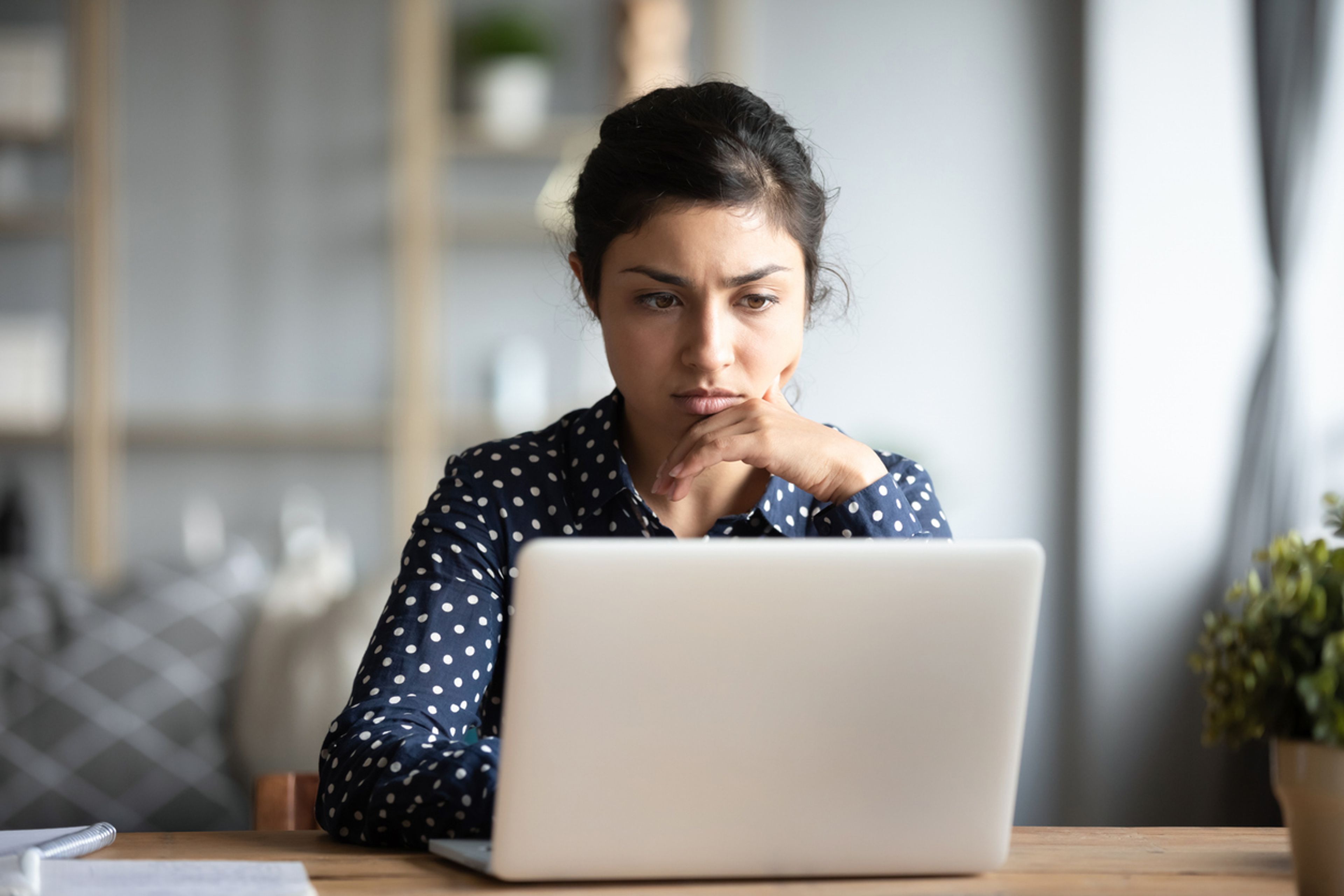Woman frowning while looking at something on her laptop screen at home.