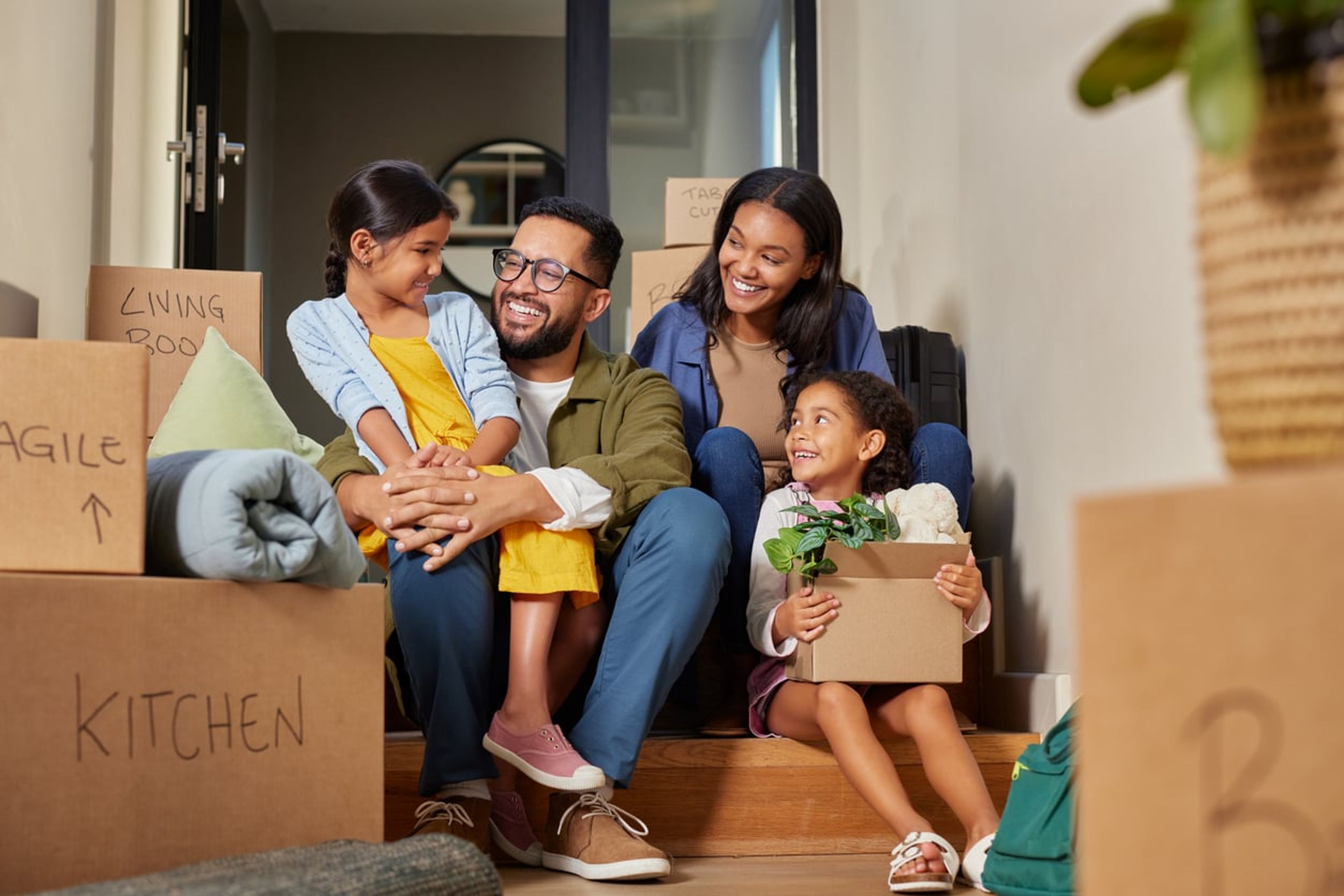 A young mother, father, and two children sit in the doorway of a house, surrounded by boxes after moving.