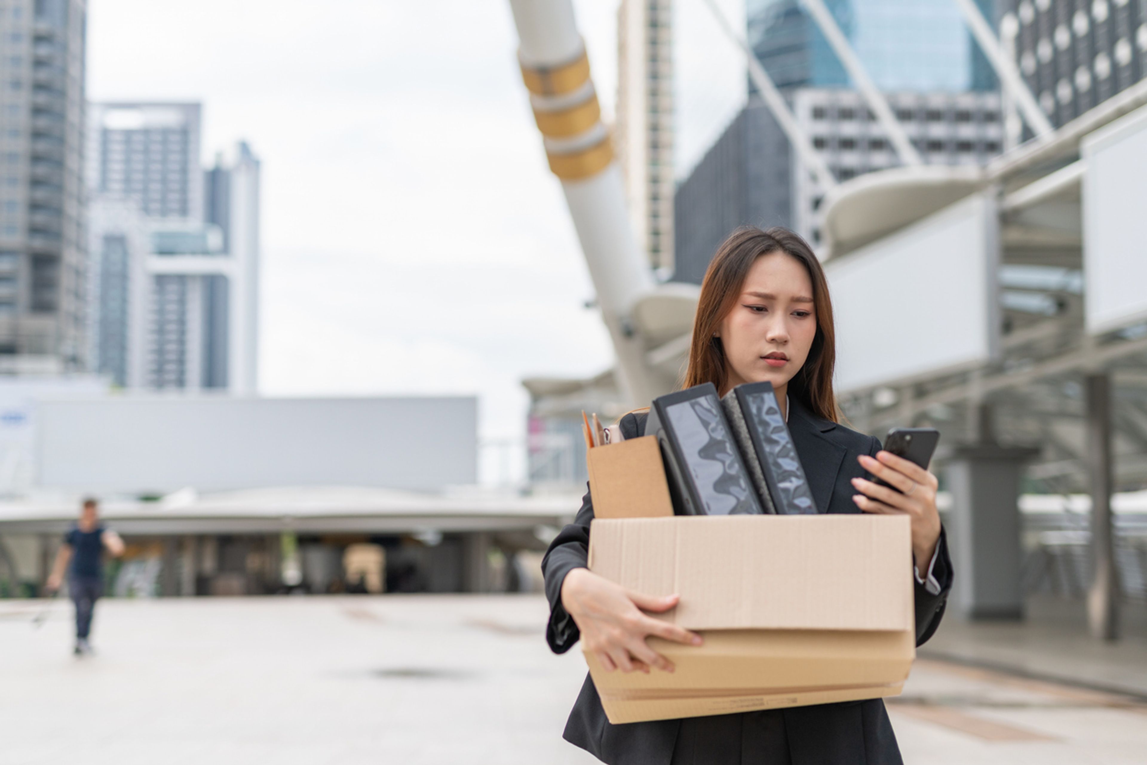 A laid-off worker outside her office carrying a box of her stuff.