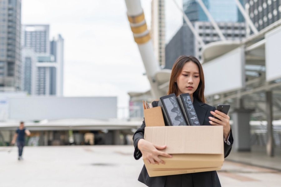 A laid-off worker outside her office carrying a box of her stuff.