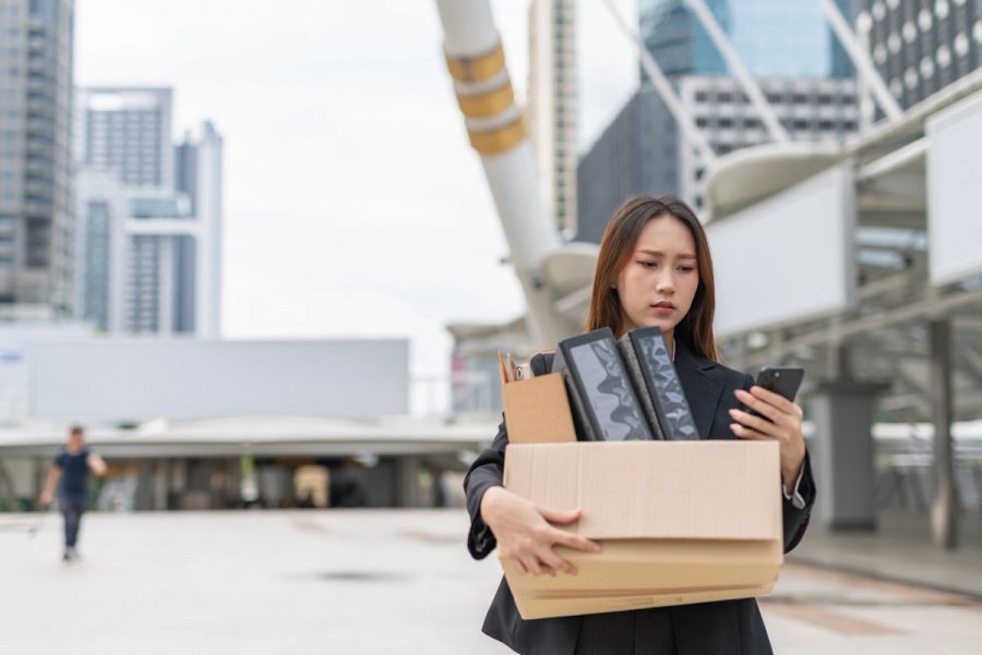 A laid-off worker outside her office carrying a box of her stuff.