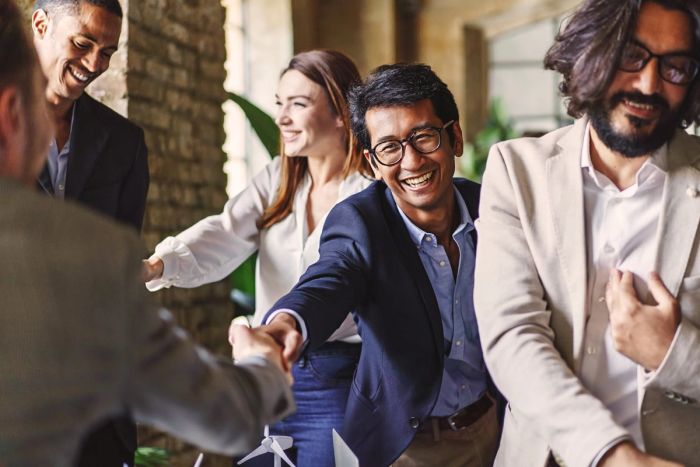A company executive in a blue jacket shakes someone's hand while smiling.