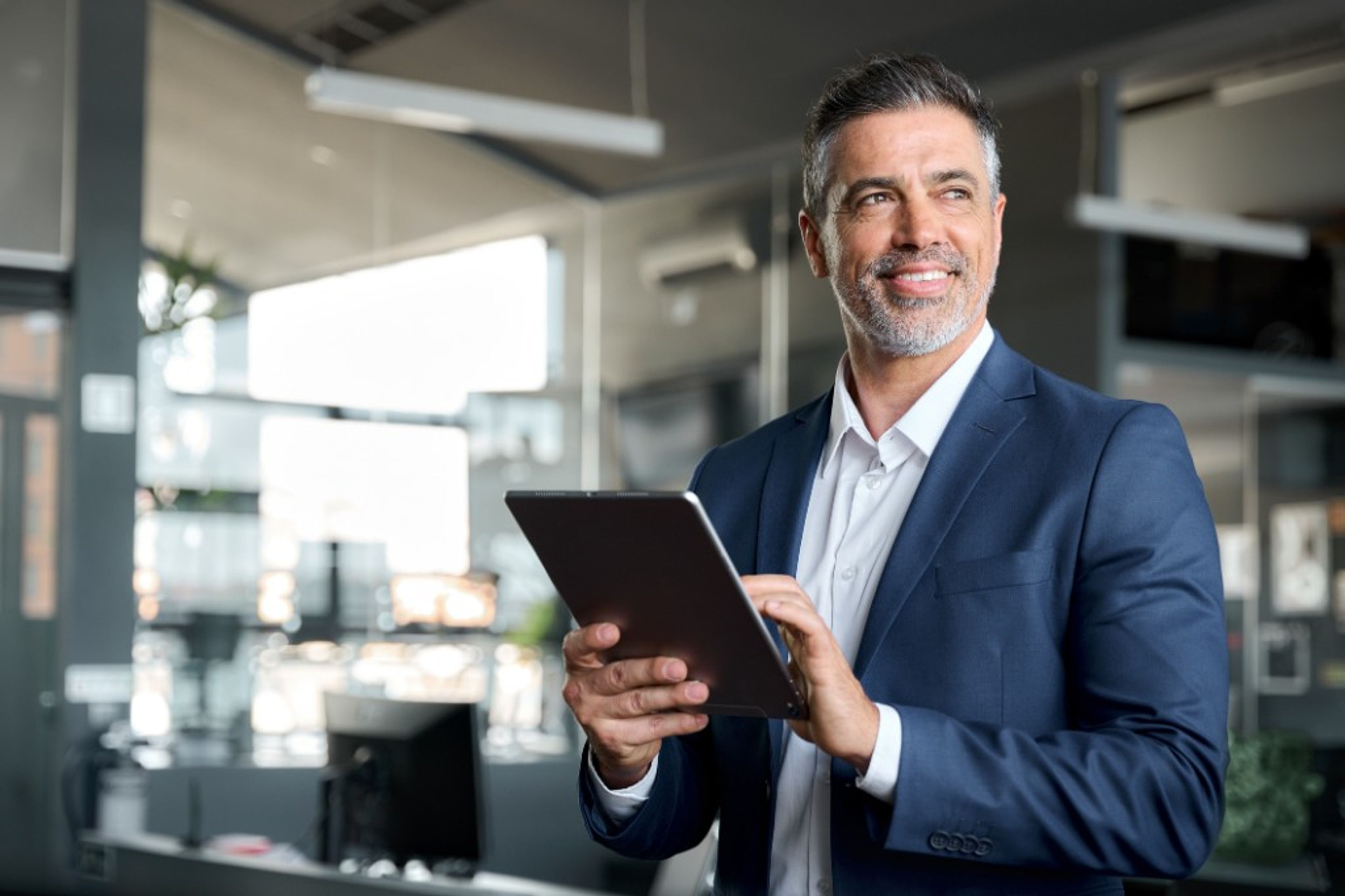 A professional in business attire holding a tablet in a modern office.