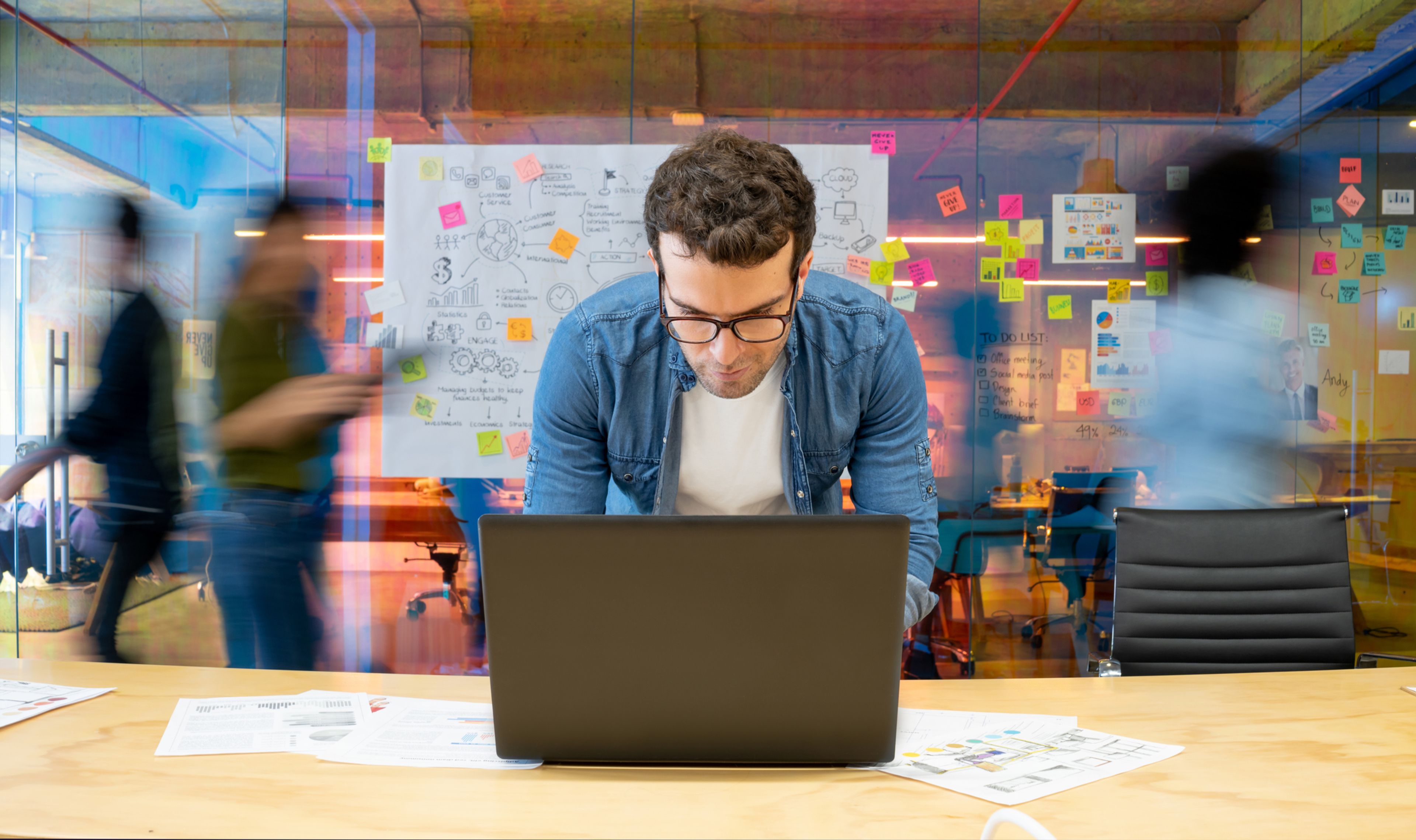 A founder working on a laptop at a desk in a busy creative office.