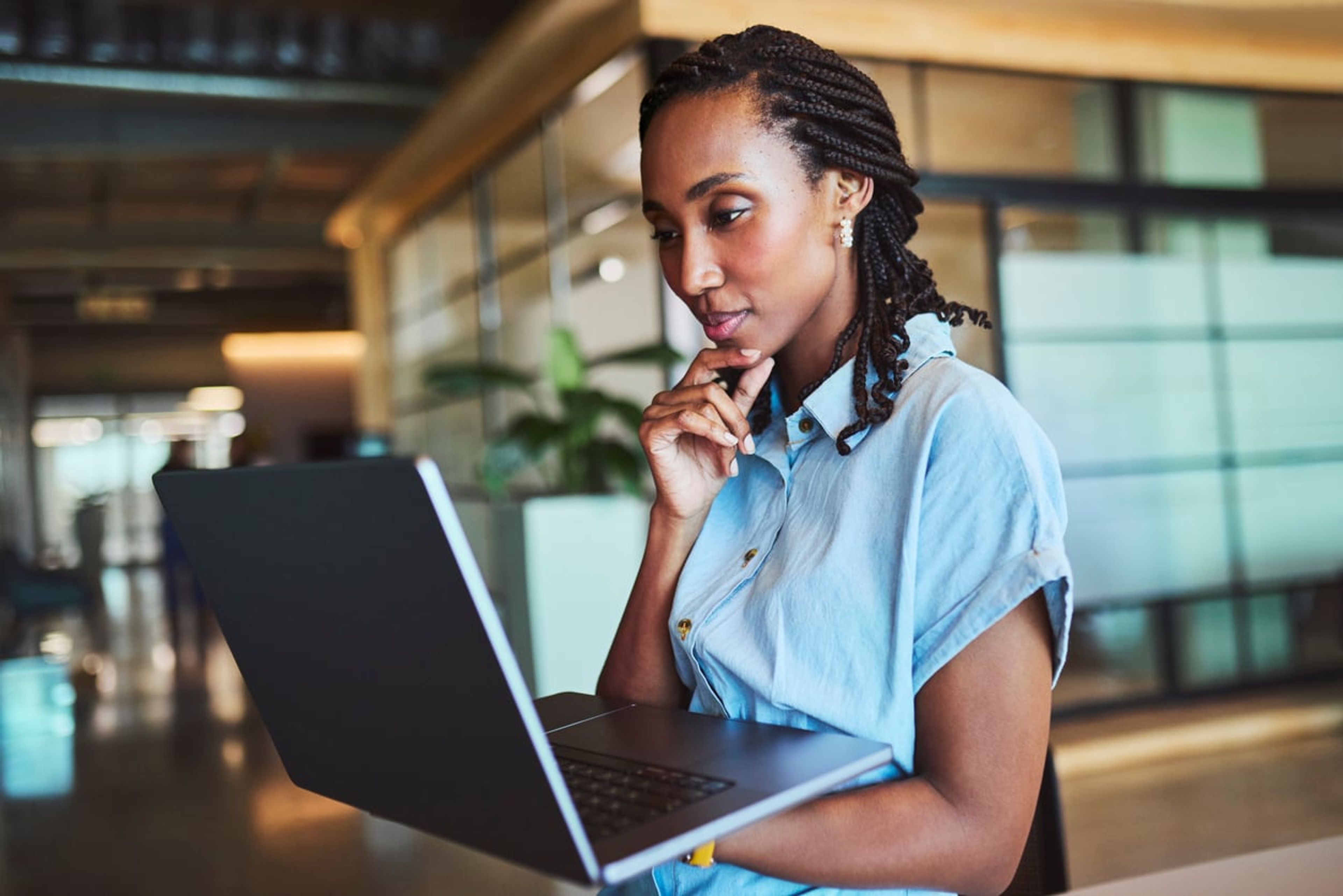 Female worker in modern office looking for information on her laptop screen.