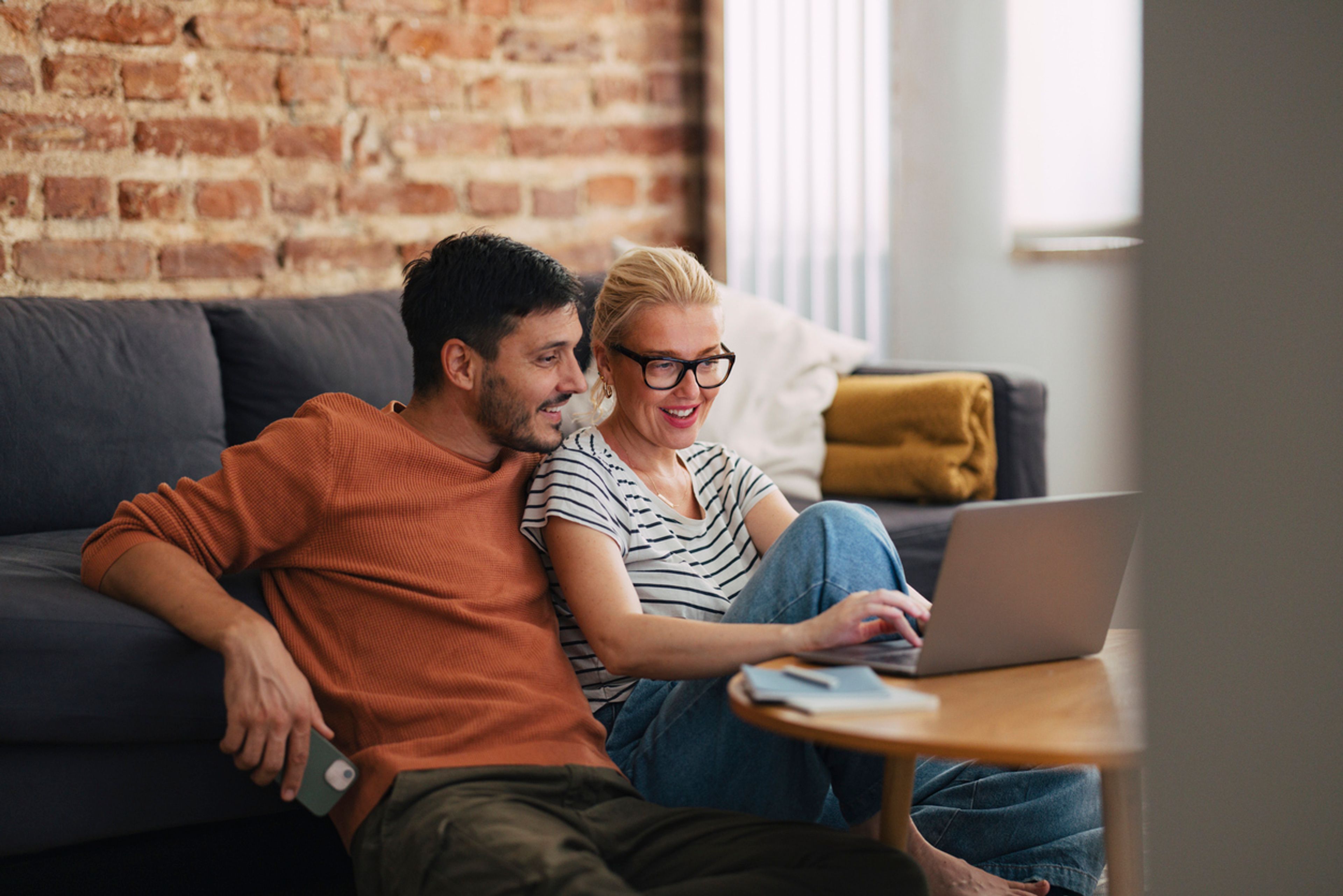 Smiling couple looking at laptop together with a notepad and pen next to the device.