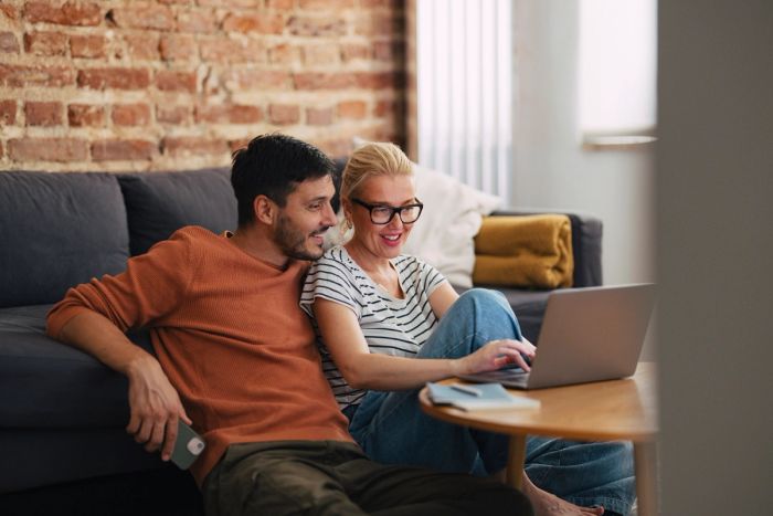 Smiling couple looking at laptop together with a notepad and pen next to the device.