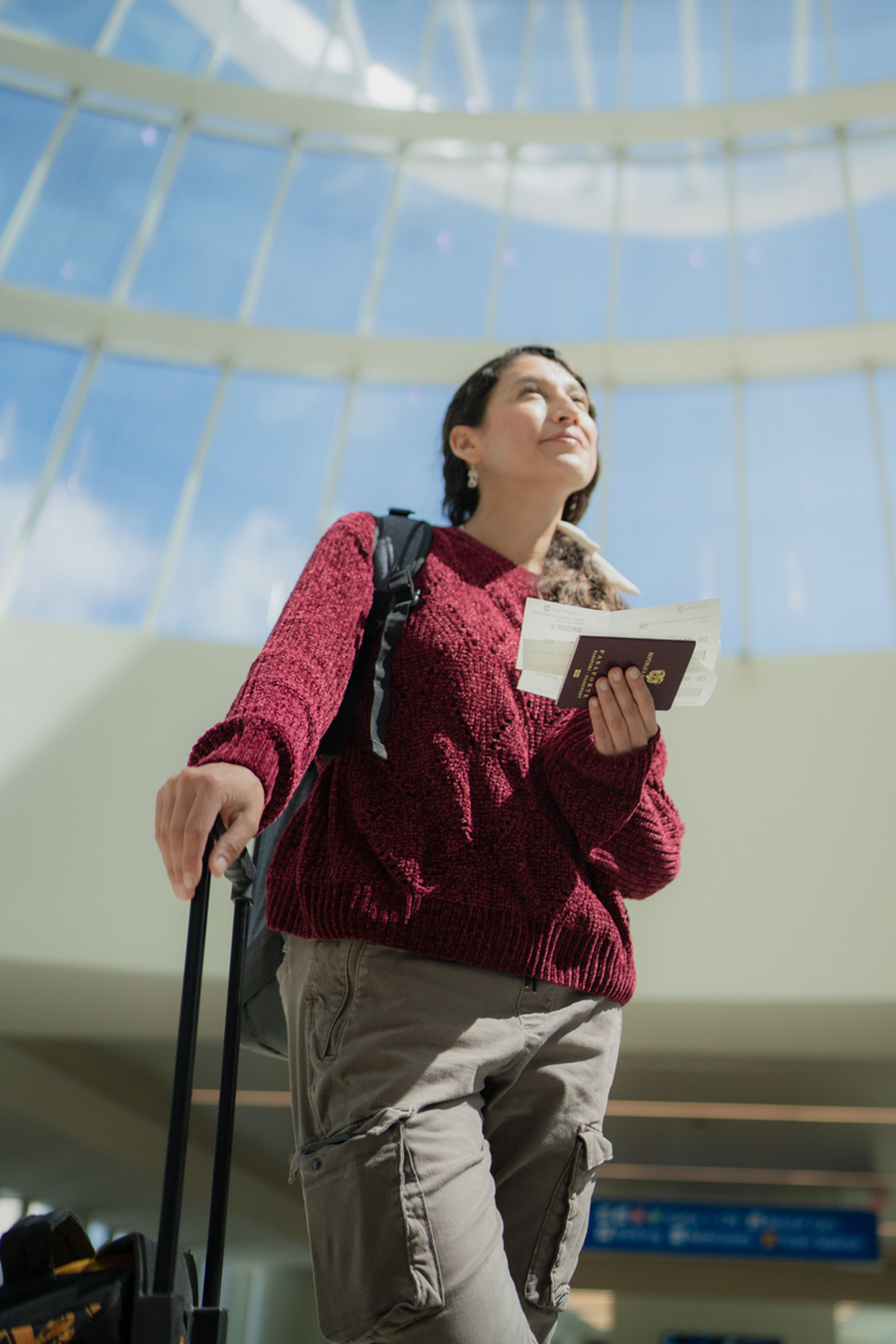 A young woman at an aiport holds her travel documents and looks upward.
