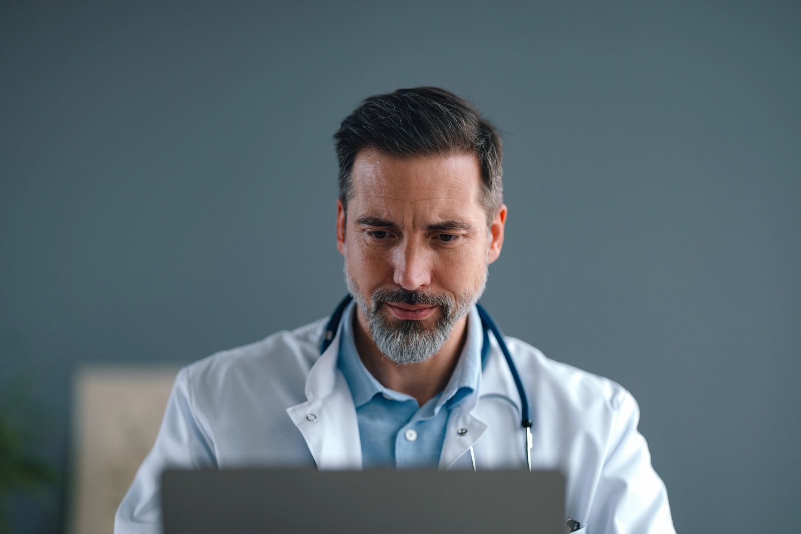 A physician reviewing case notes at a laptop