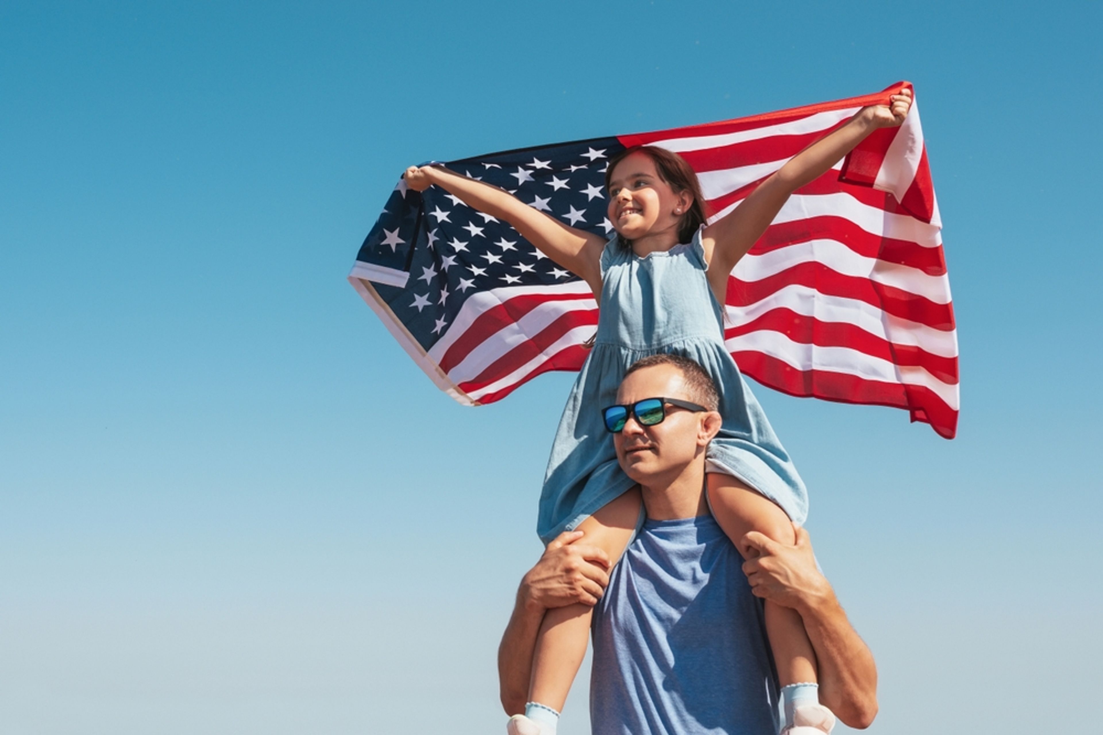 Father with daughter on his shoulders holding an American flag.