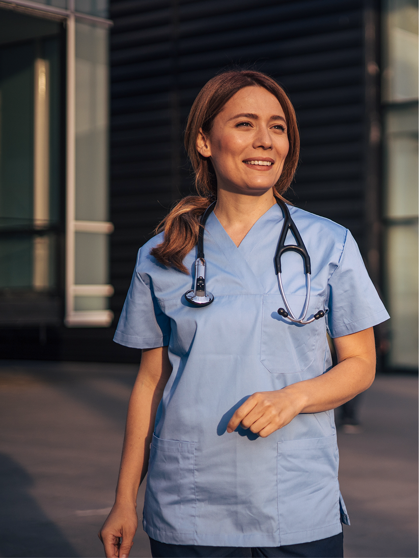 A physician in scrubs smiling outdoors
