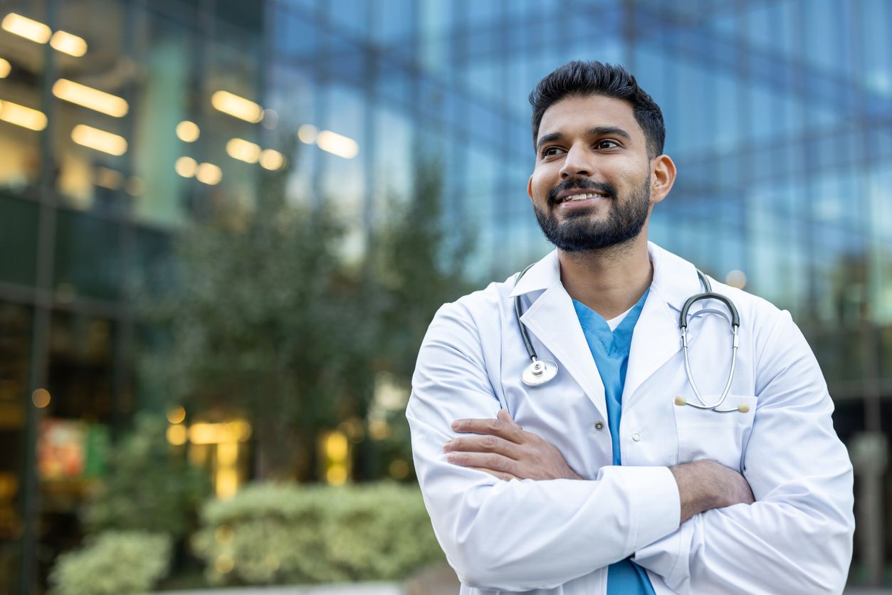 A confident doctor in a white coat smiling while standing outside near a modern building.