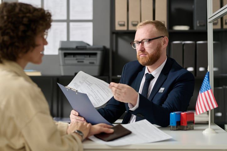 A bearded male worker in an immigration office checks someone's O-1 visa renewal application.