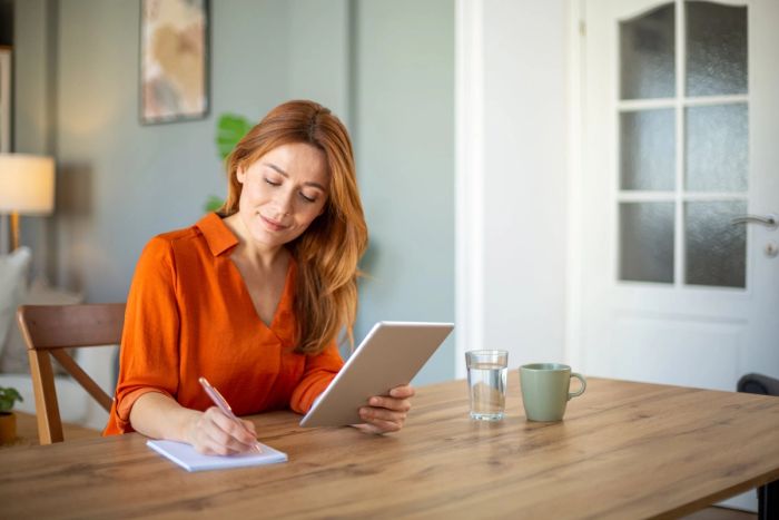 A woman sits at a desk smiling while holding a tablet and taking notes on the cost of a TN visa.