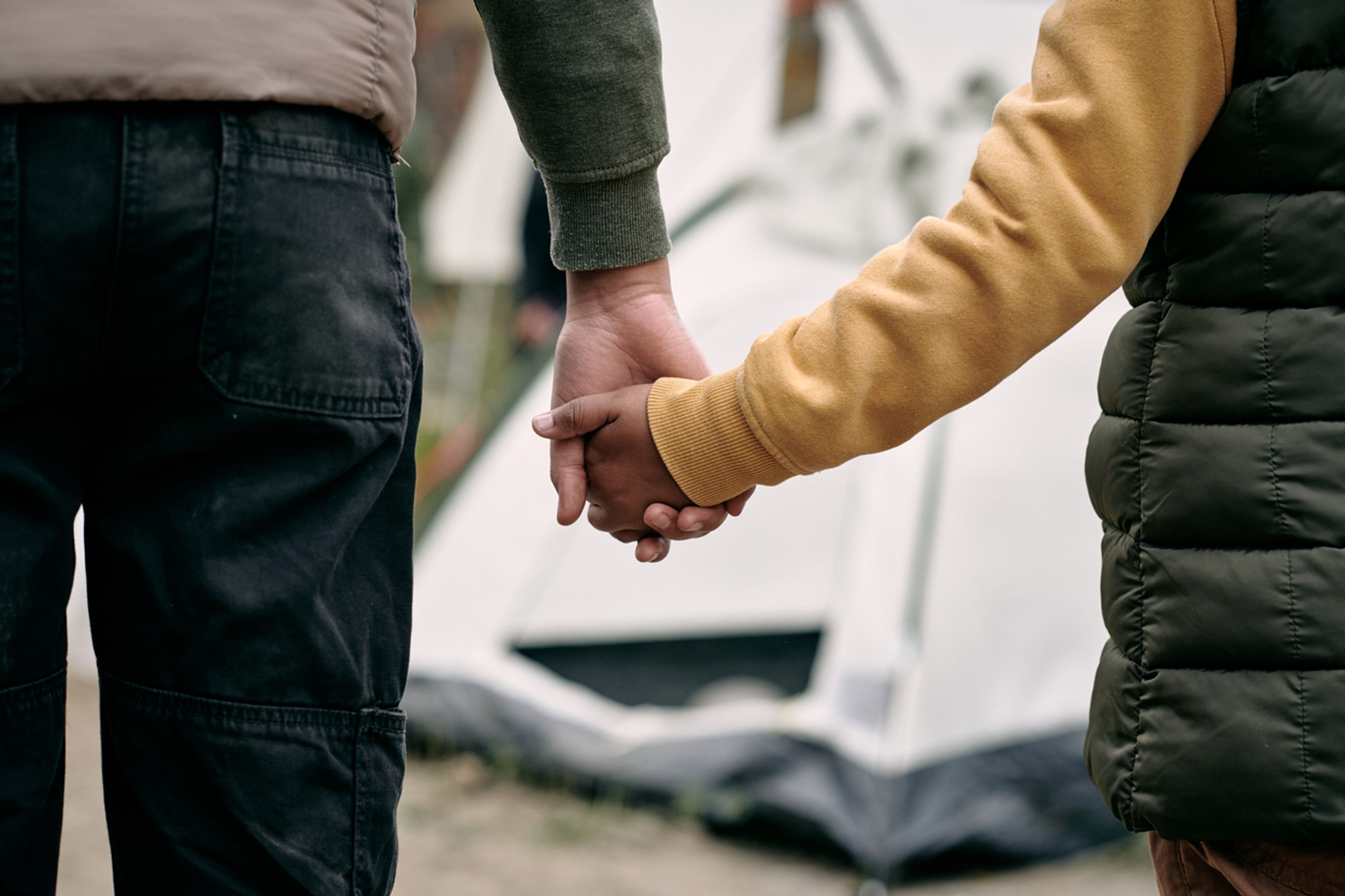 Closeup of a parent holding the hand of a child living in a migrant camp.
