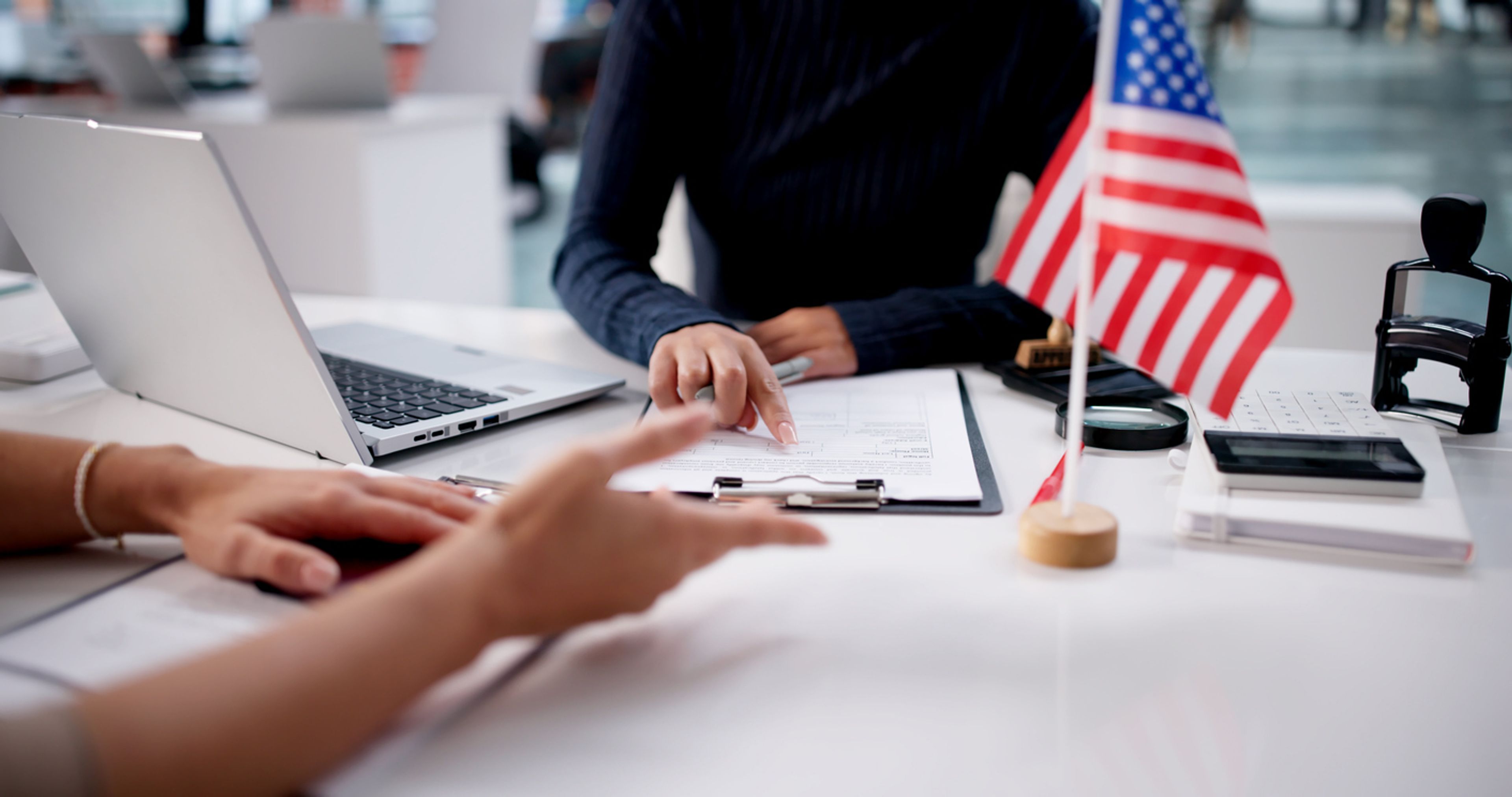 The hands of woman who are sitting at a desk discussing an immigrant visa application