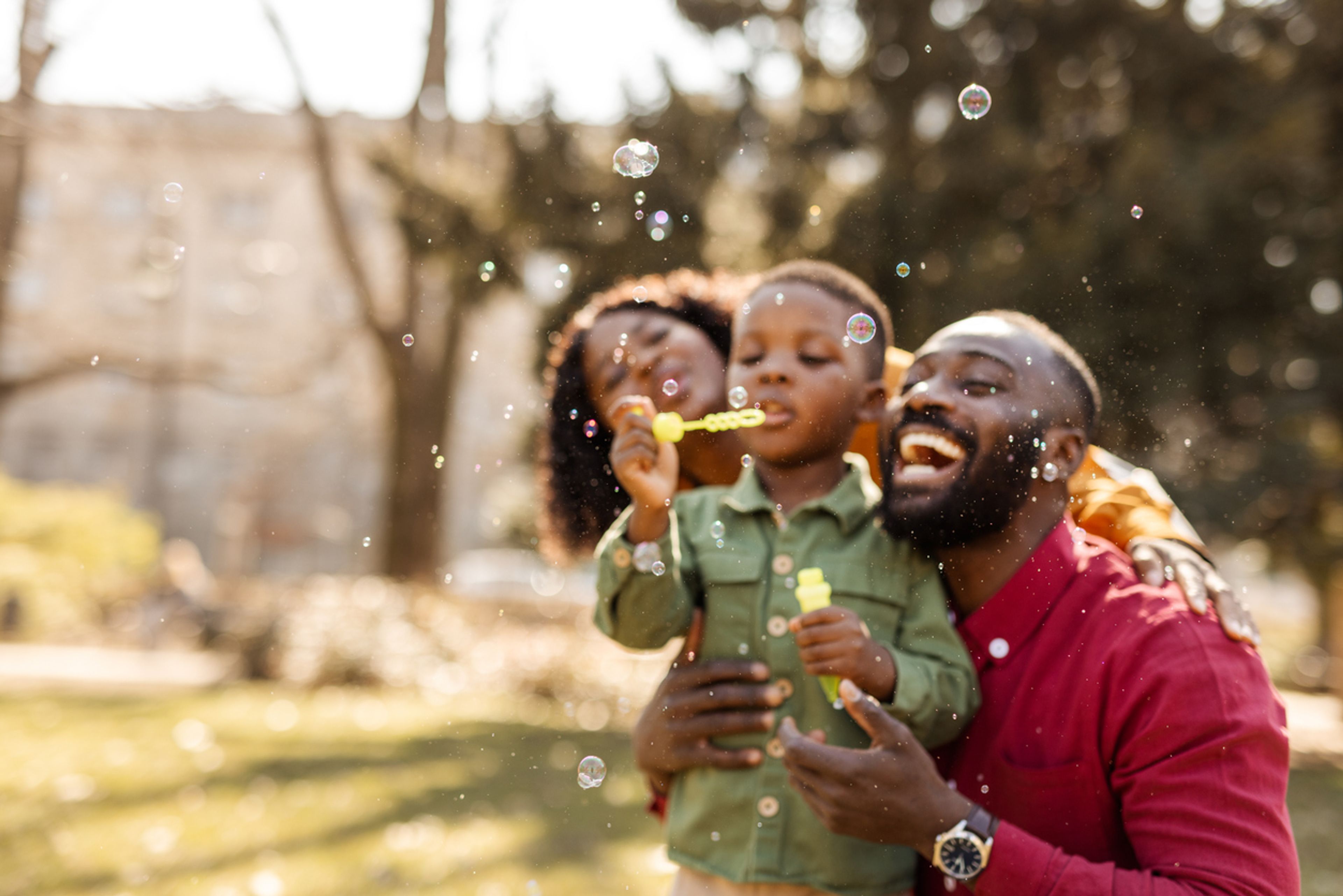 Happy family in the park with a young child blowing bubbles.