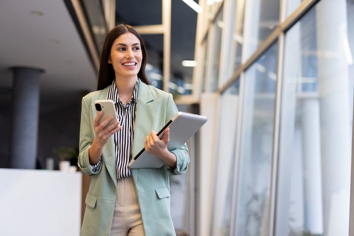 Female executive in a modern office holding her tablet and phone.