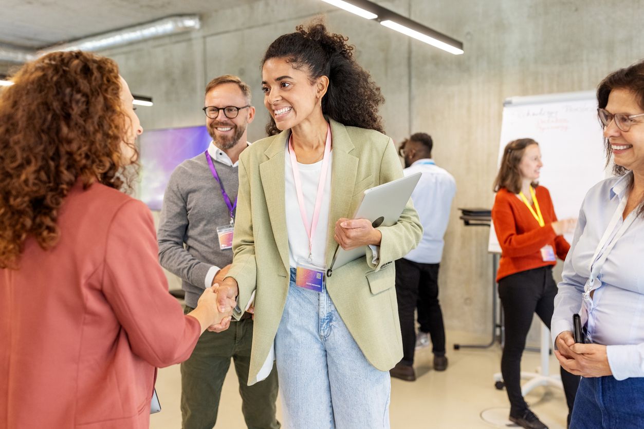 Two women shake hands while surrounded by other tech workers.