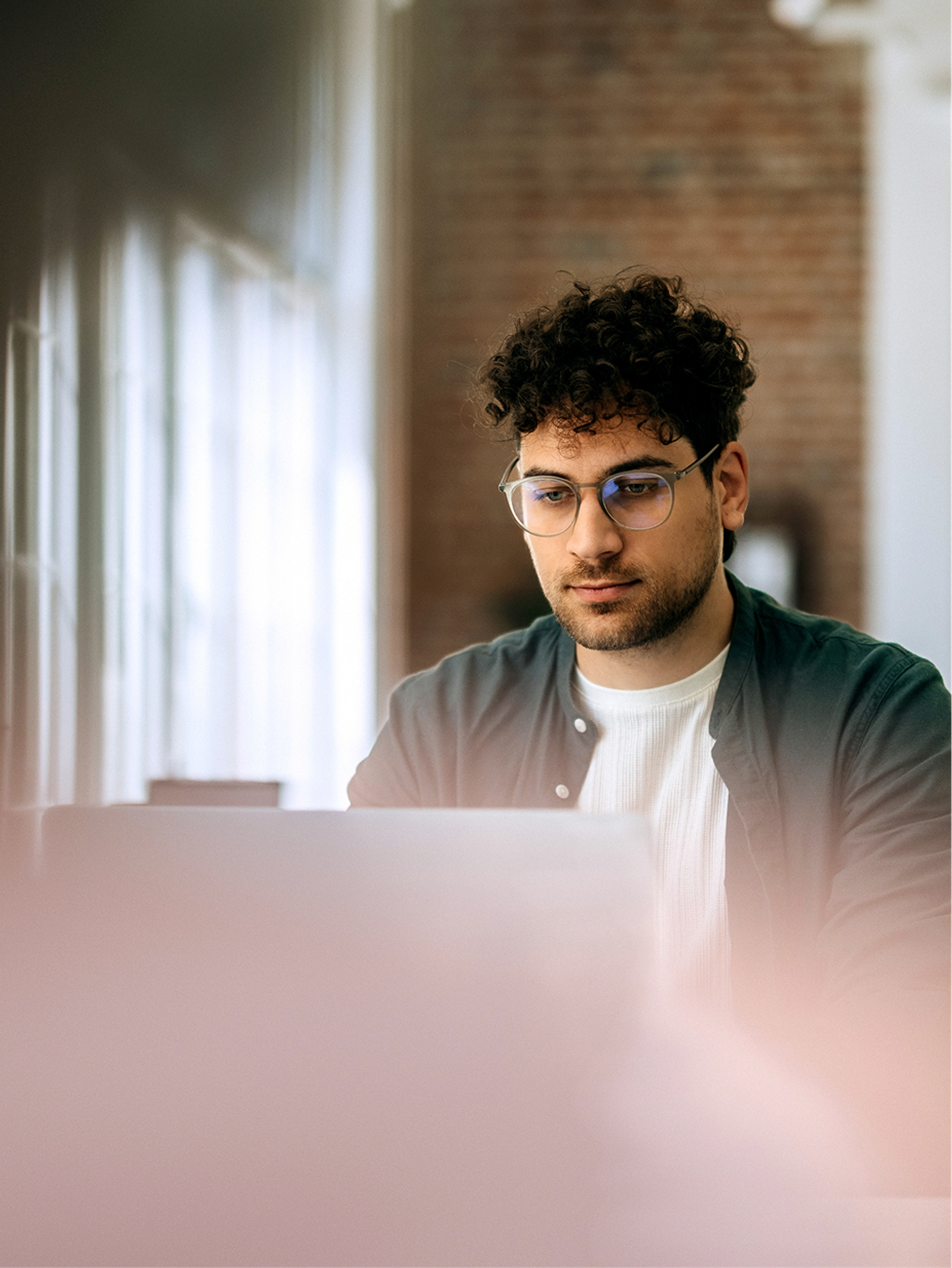 An engineer with glasses working on a laptop in a bright office
