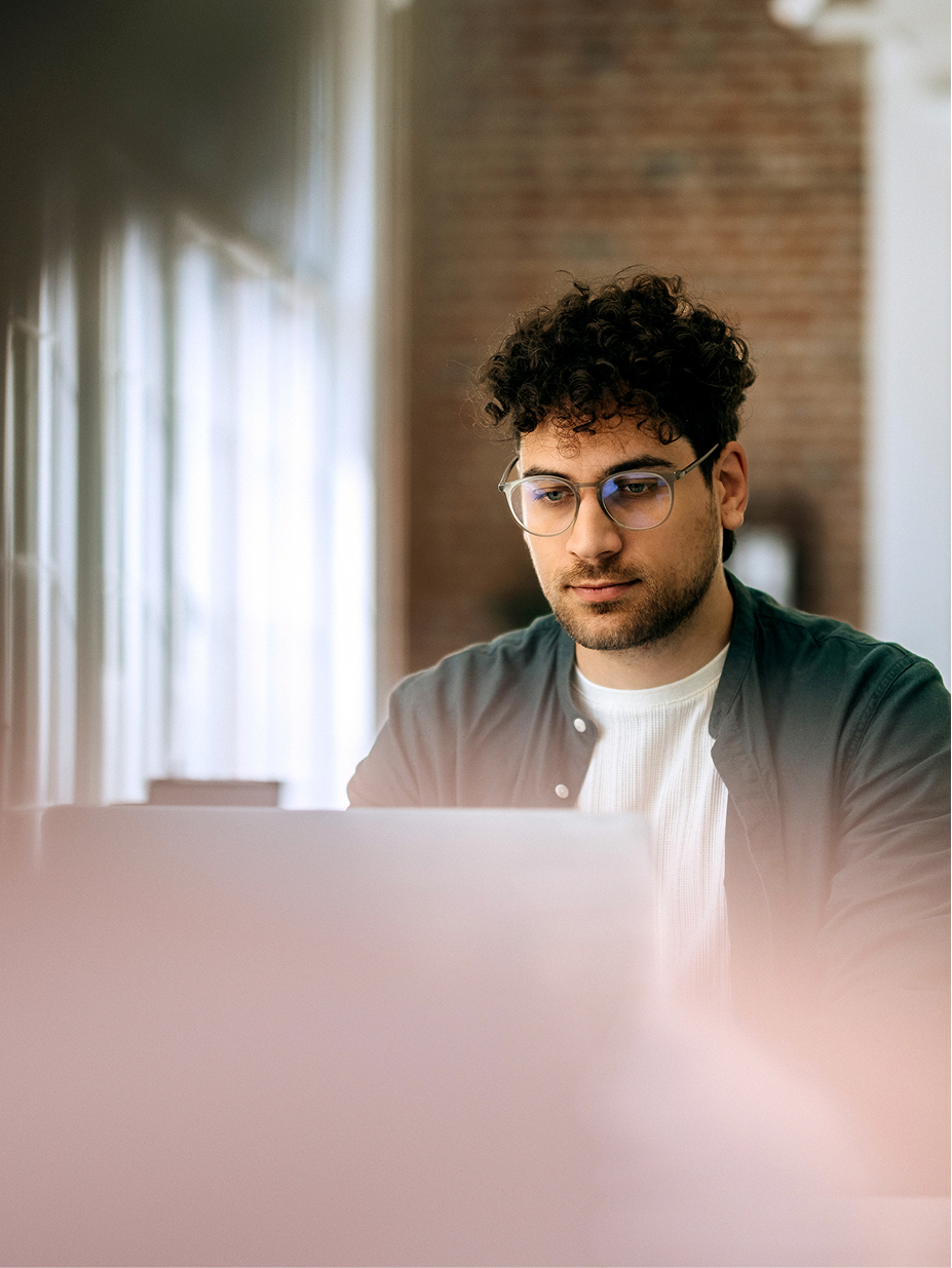 An engineer with glasses working on a laptop in a bright office