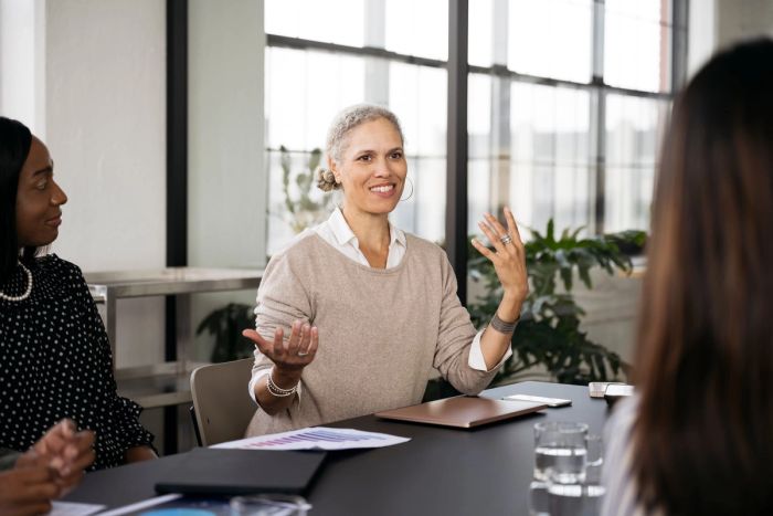 A mature professional woman gestures that she is weighing two options during a business meeting.