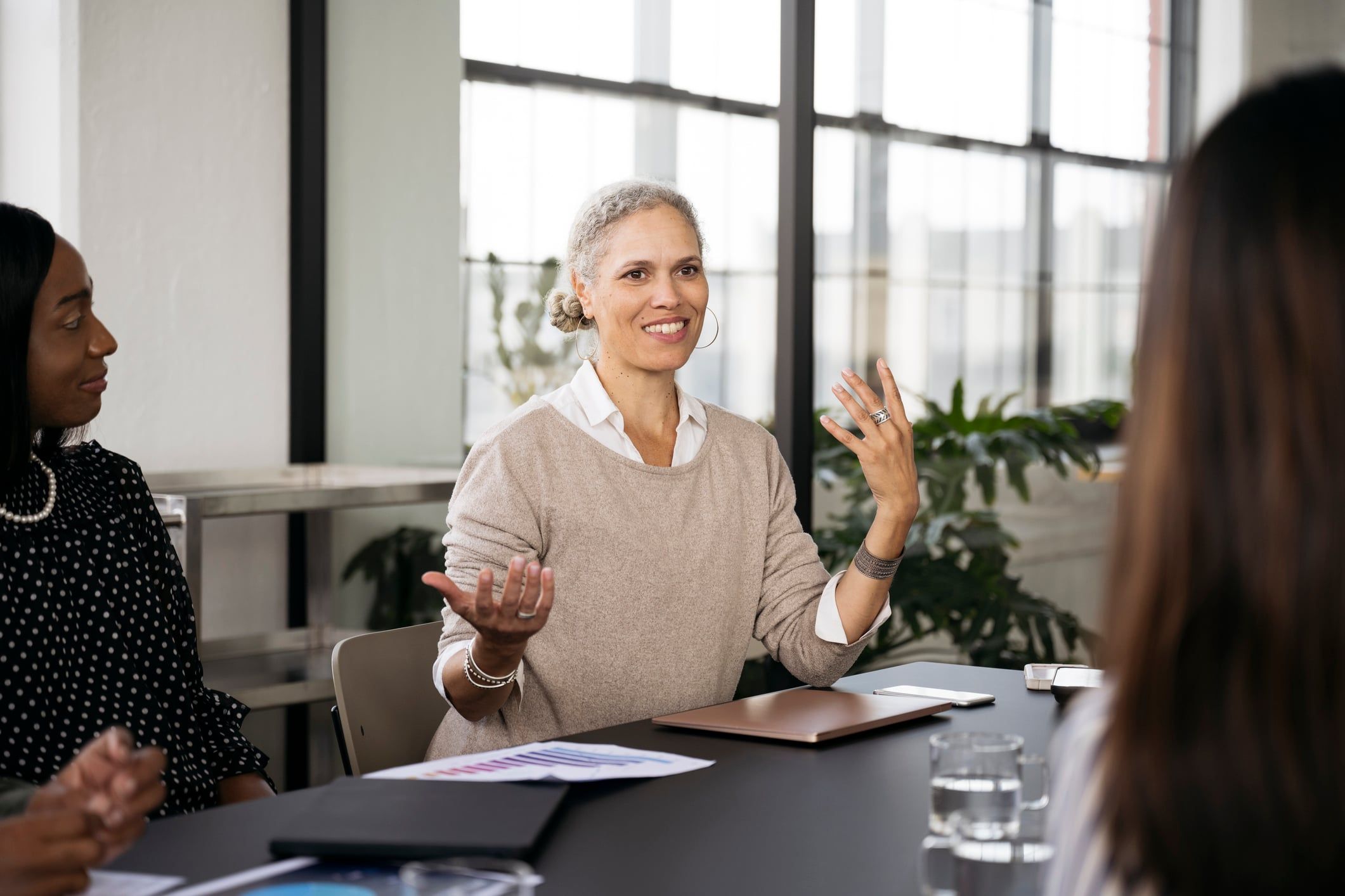 A mature professional woman gestures that she is weighing two options during a business meeting.